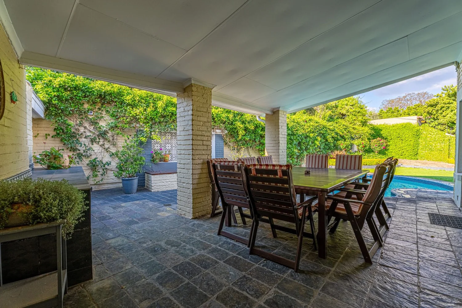 The covered patio with a long timber table, looking out across the lawn to the pool
