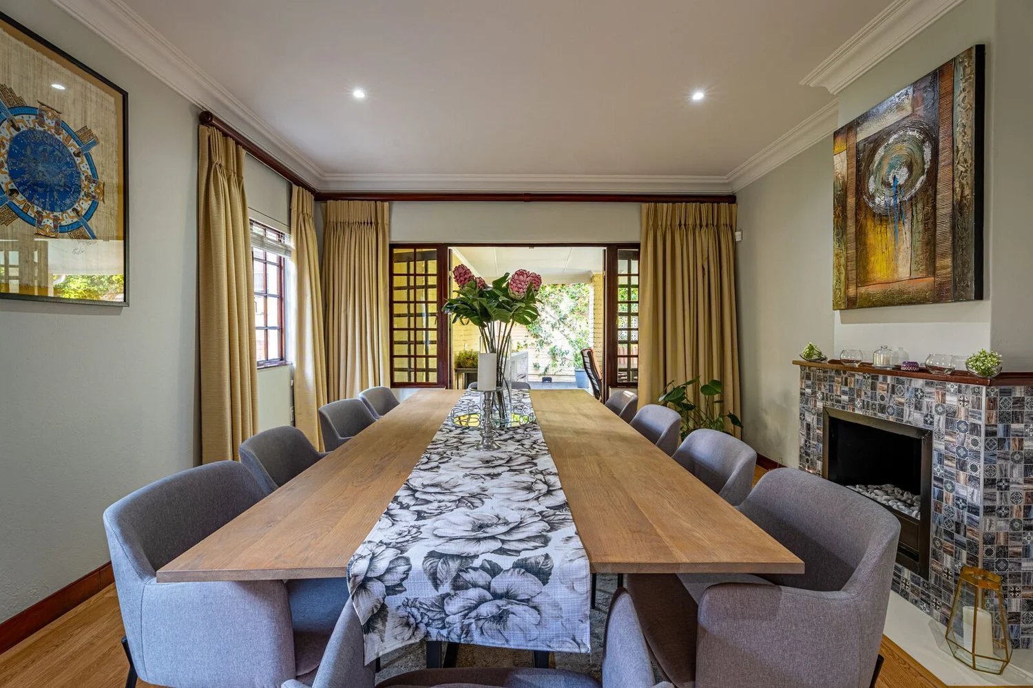 Dining room with a long timber table seating ten, a tiled fireplace and glazed doors onto the garden