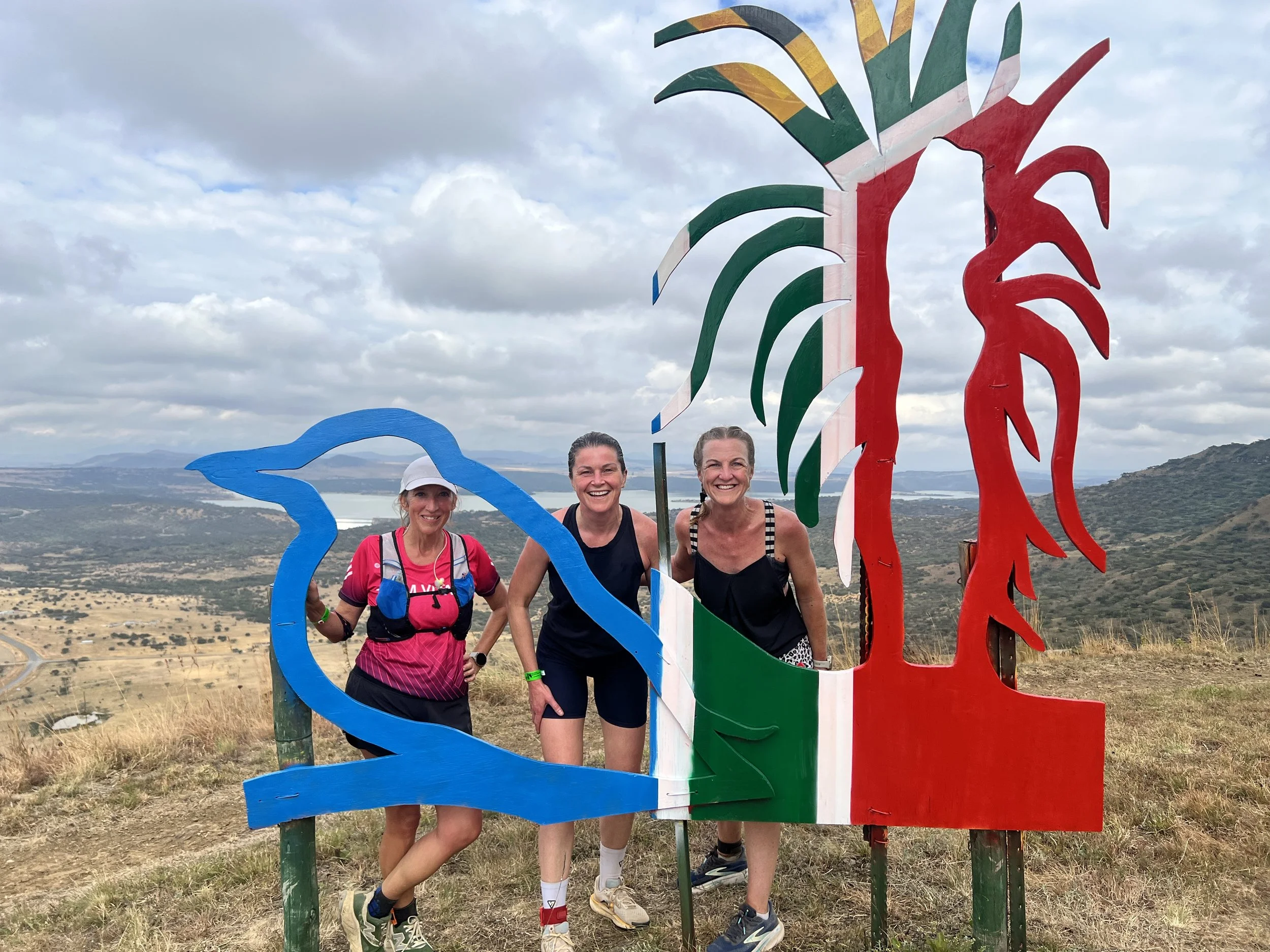 Three friends on a hike beside a colourful South African flag sculpture