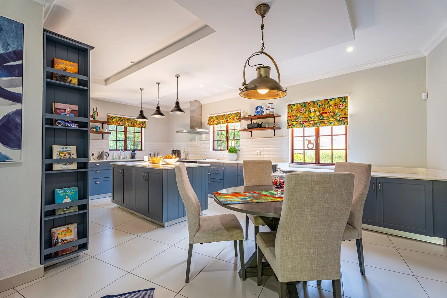 Kitchen with deep slate blue Shaker cabinetry, white worktops, an island and a breakfast table under pendant lights