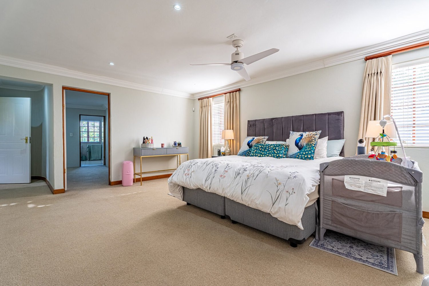 The main bedroom, a carpeted corner room with afternoon light and a door through to the en suite