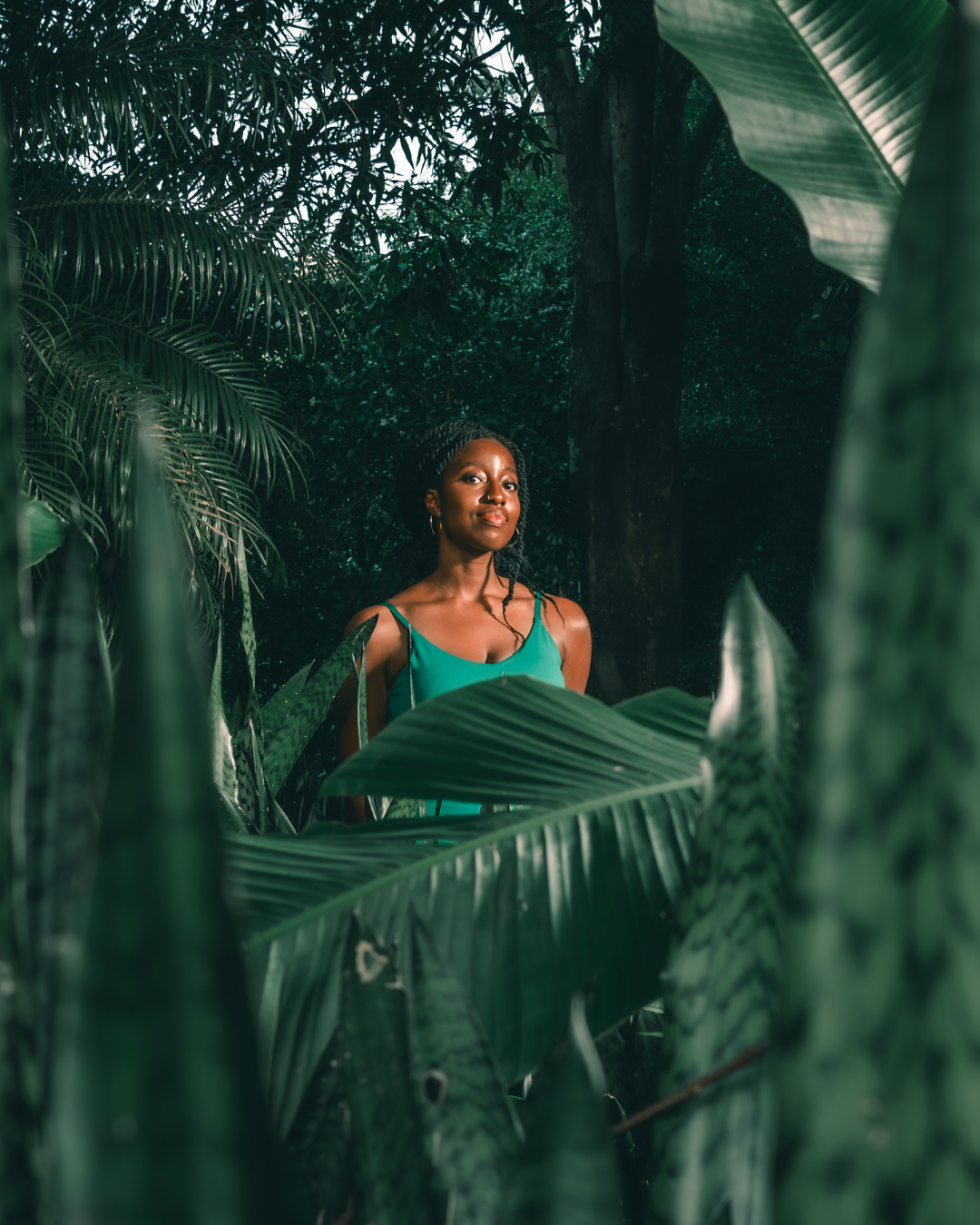 Biola Jeje standing among palm leaves, looking directly at camera
