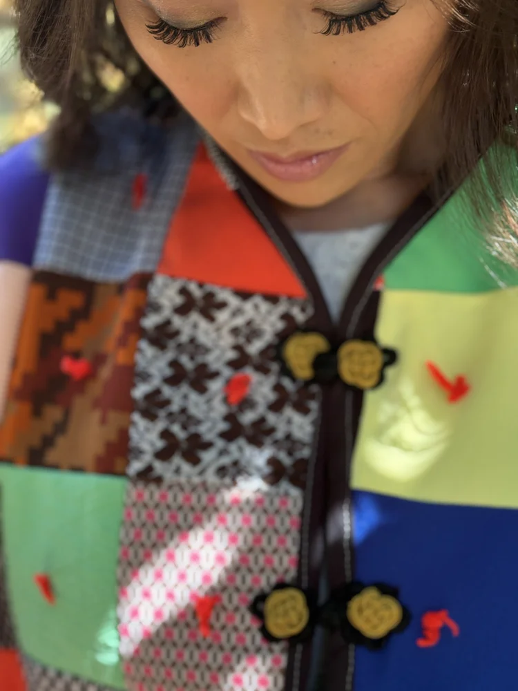 One-of-one jacket made from a second-hand patchwork quilt, preserving its original mix of color, pattern and hand-tied red yarn knots throughout. Finished with black binding, decorative closures, and a contrasting vintage 1970s floral lining in lime 