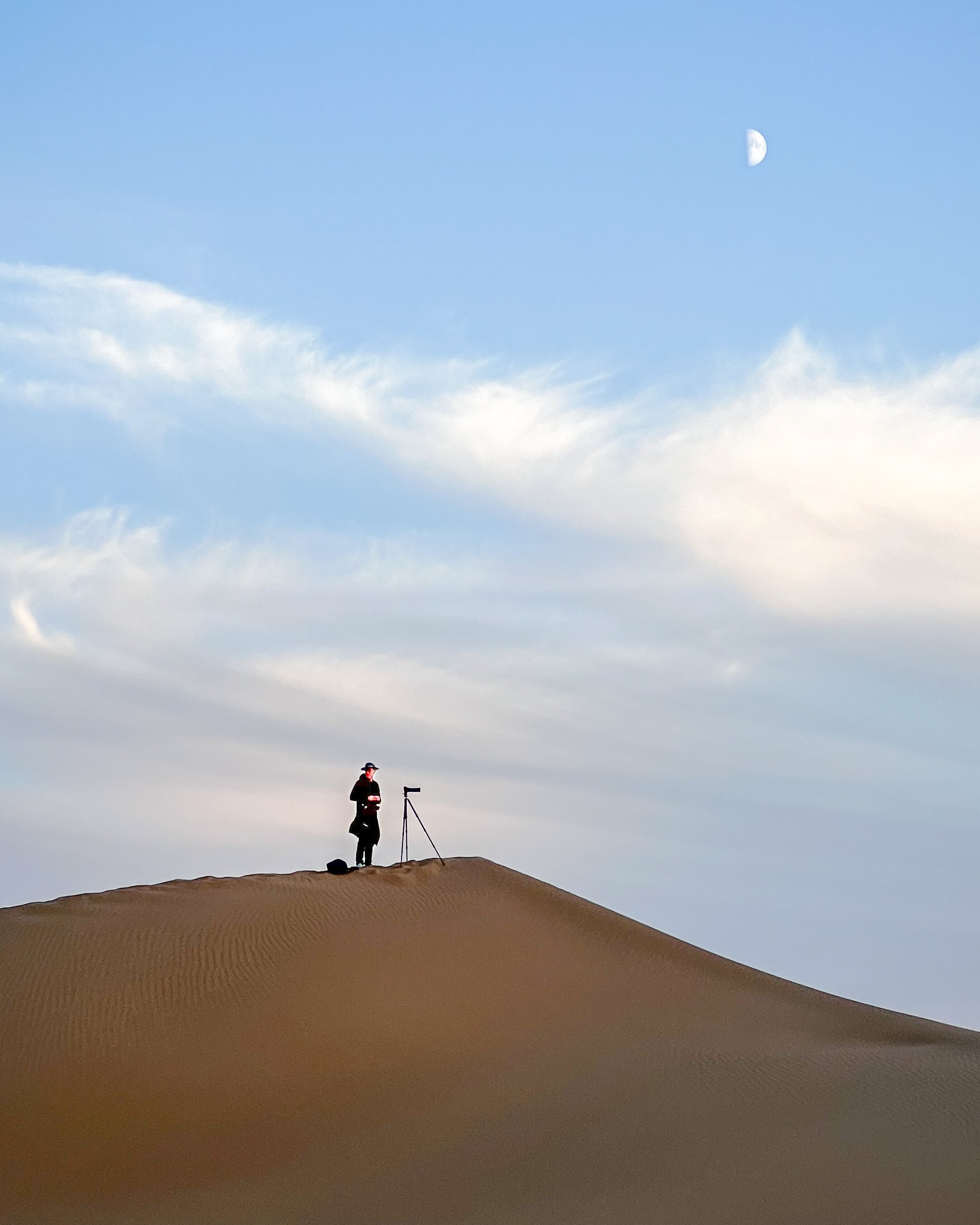 Manfred Schuster with tripod on a desert dune, small figure under a vast sky