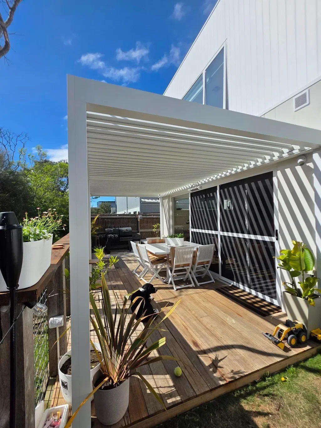 White louver pergola attached to a house over a timber deck