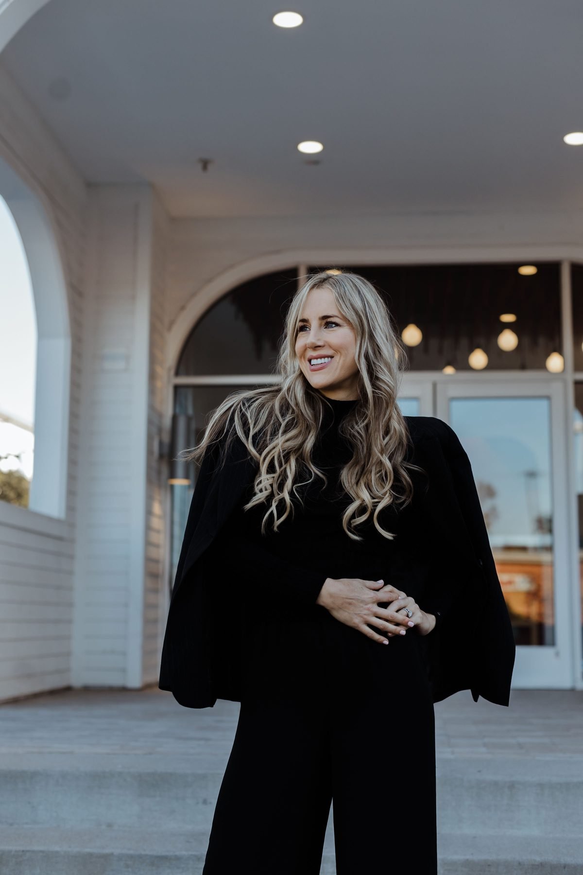 Megan Bruneau in a black outfit, smiling, in front of a white arched building