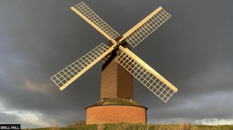 Brick windmill with four white sails against  dramatic dark grey clouds.