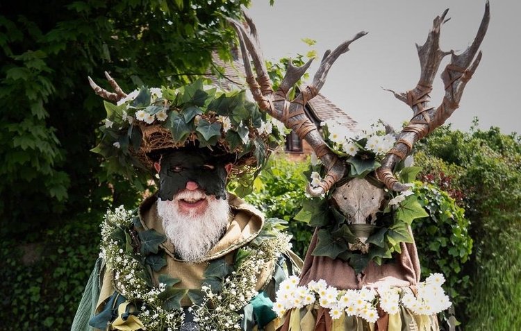 Green Man garlanded with leaves and flowers carrying decorated deer antlers 