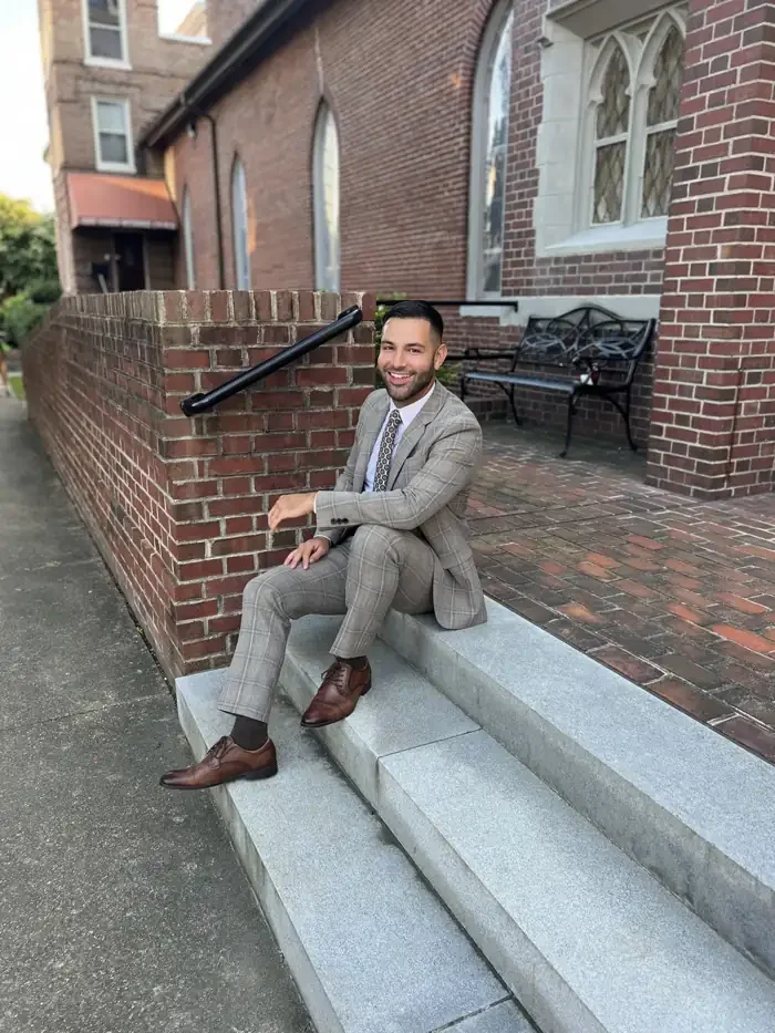 Anthony, founder of Anticipated Events, smiling on brick steps in a tan plaid suit