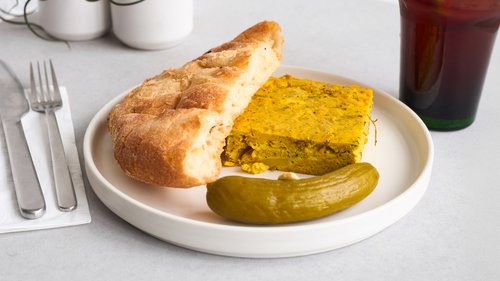 Saffron chicken fritata on a plate with bread and a cucunber pickle