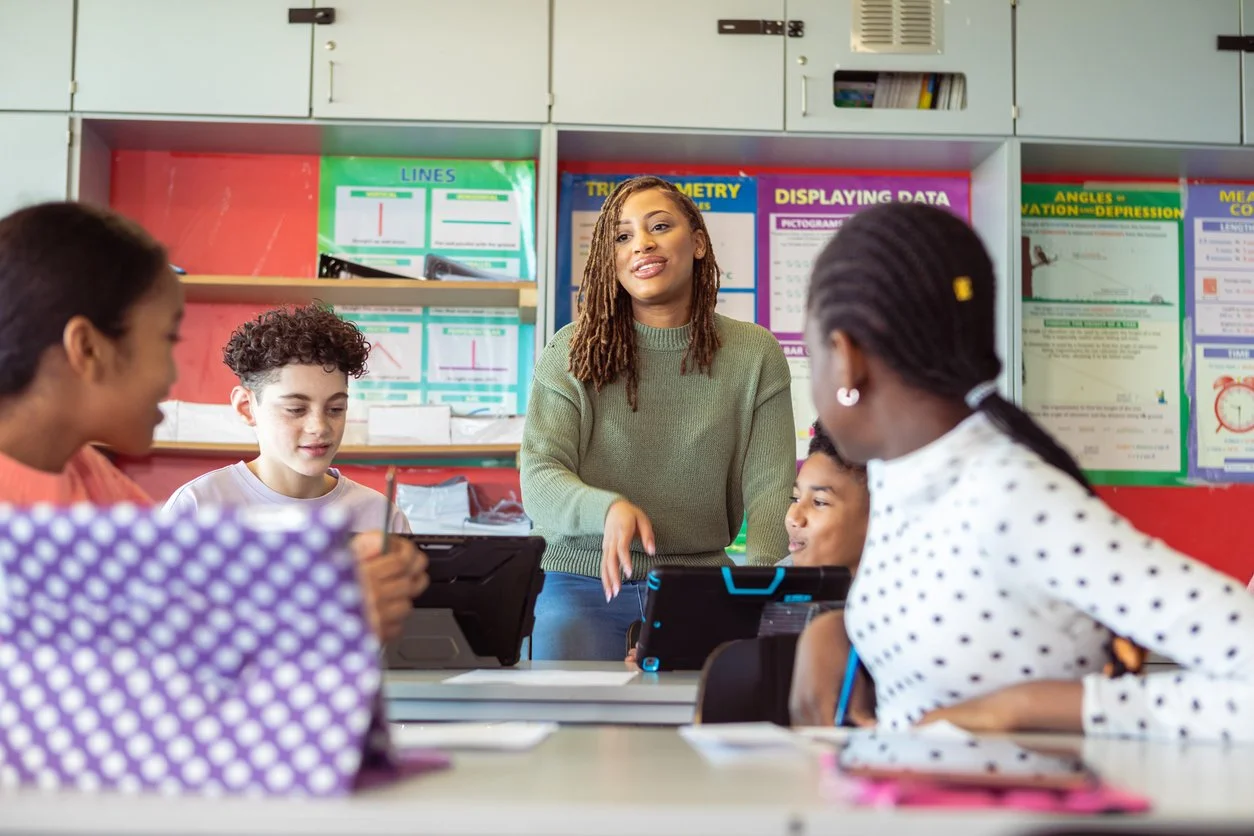 A teacher talking with students working together in a classroom.