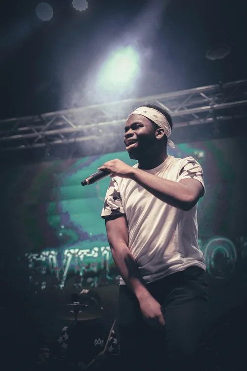 ELAM student performing on stage with a microphone under a spotlight