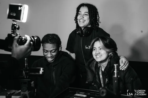 Three students laughing around a camera in black and white