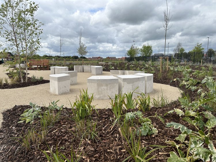 a garden with stone and terrazzo block benches in a circle surrounded by newly planted gardens