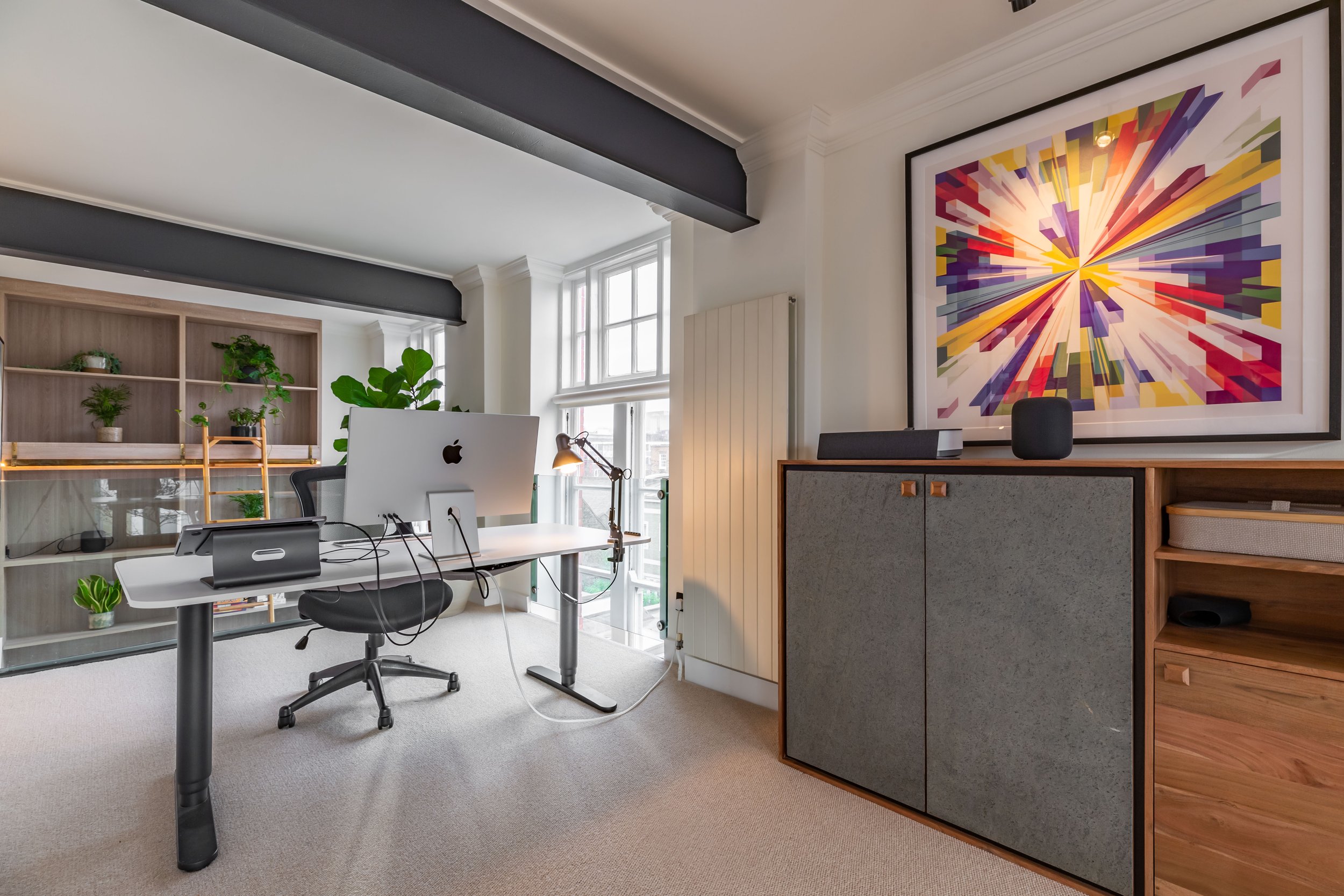 Mezzanine home office in a Grade II listed school conversion London — original wrought iron beams painted dark and left exposed, glass balustrade, bespoke oak sideboard, original sash windows. Modern heritage interior design by Studio Akiva