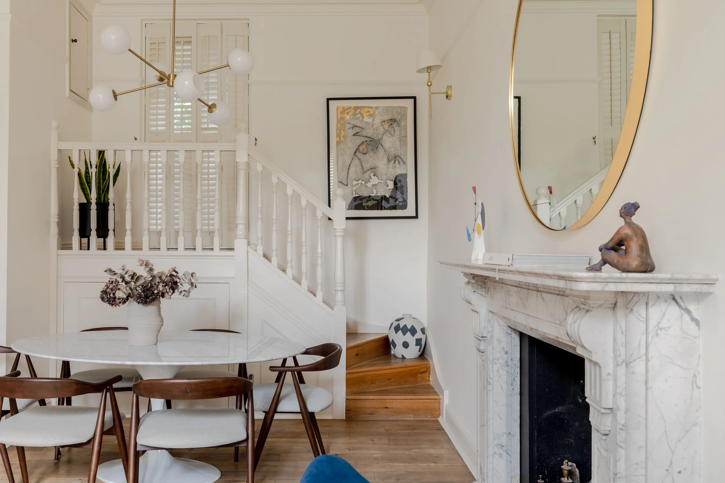 Victorian terraced house dining room with original marble fireplace, staircase beyond, mid-century dining furniture, art collection, herringbone oak floor. Modern heritage interior design by Studio Akiva