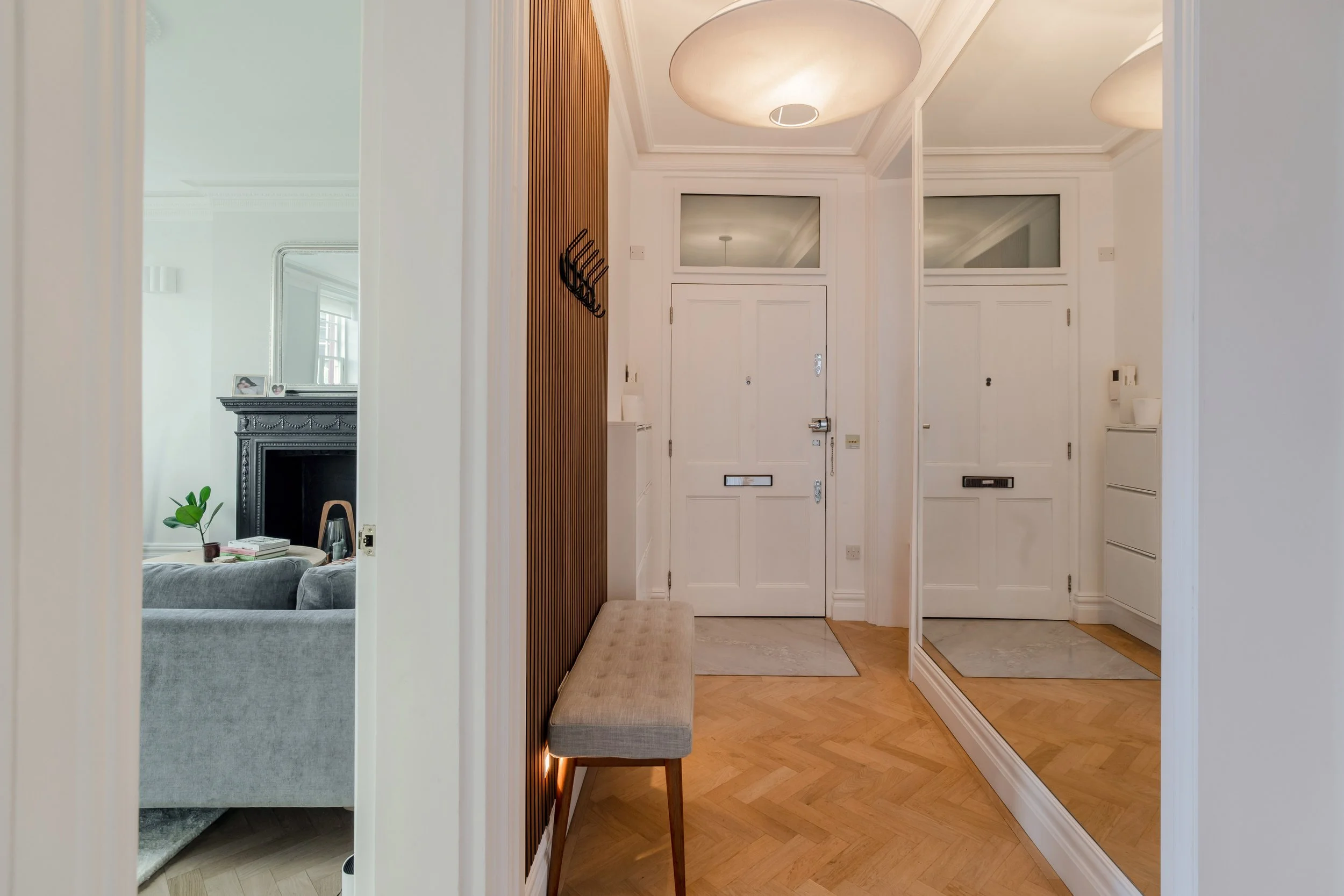 Minimal contemporary hallway with herringbone flooring, mirrored wardrobe, wood slat detailing, and soft ambient lighting.
