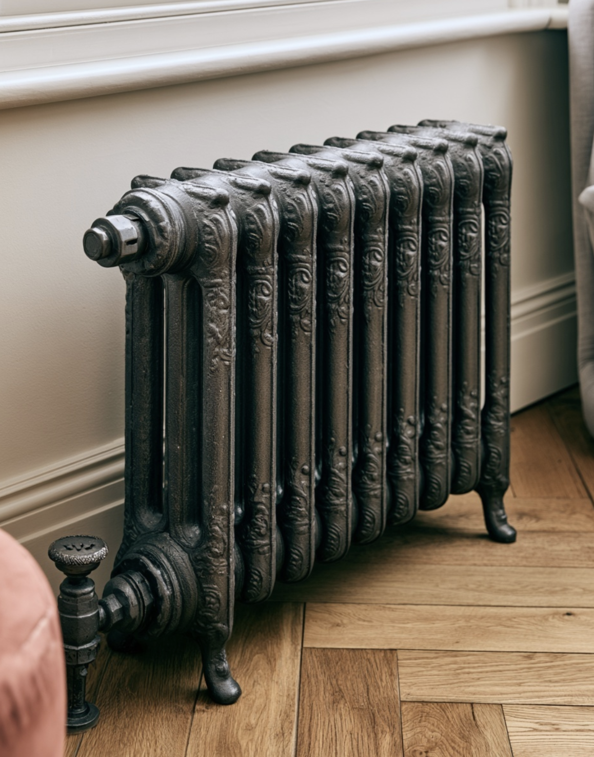 Close-up of an ornate Victorian cast iron radiator with decorative detailing, standing on herringbone parquet flooring against a pale wall