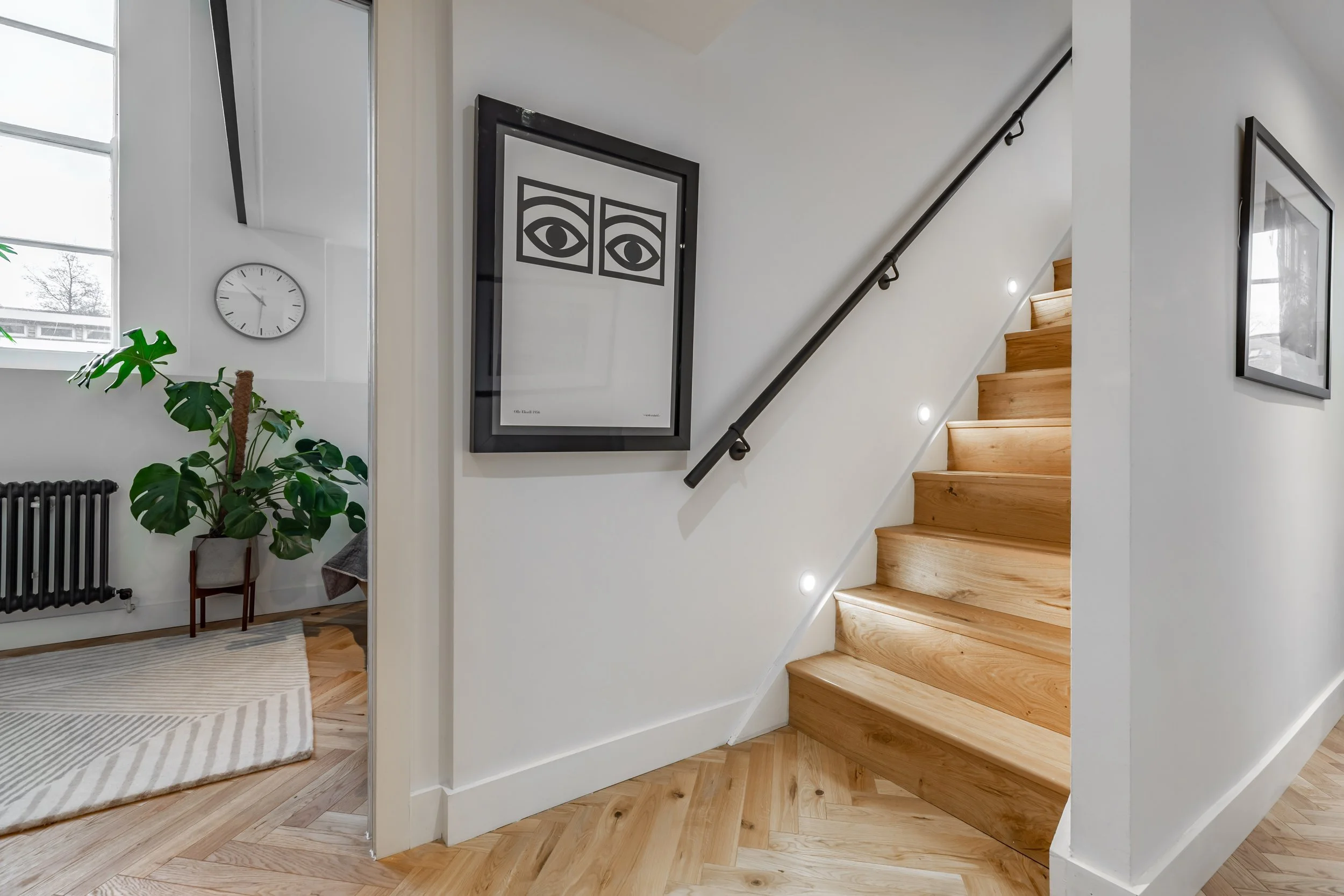 Staircase in a modernised Grade II listed London duplex — solid oak treads with recessed step lighting, matte black wall-mounted handrail, herringbone oak parquet floor below. Modern heritage interior design by Studio Akiva