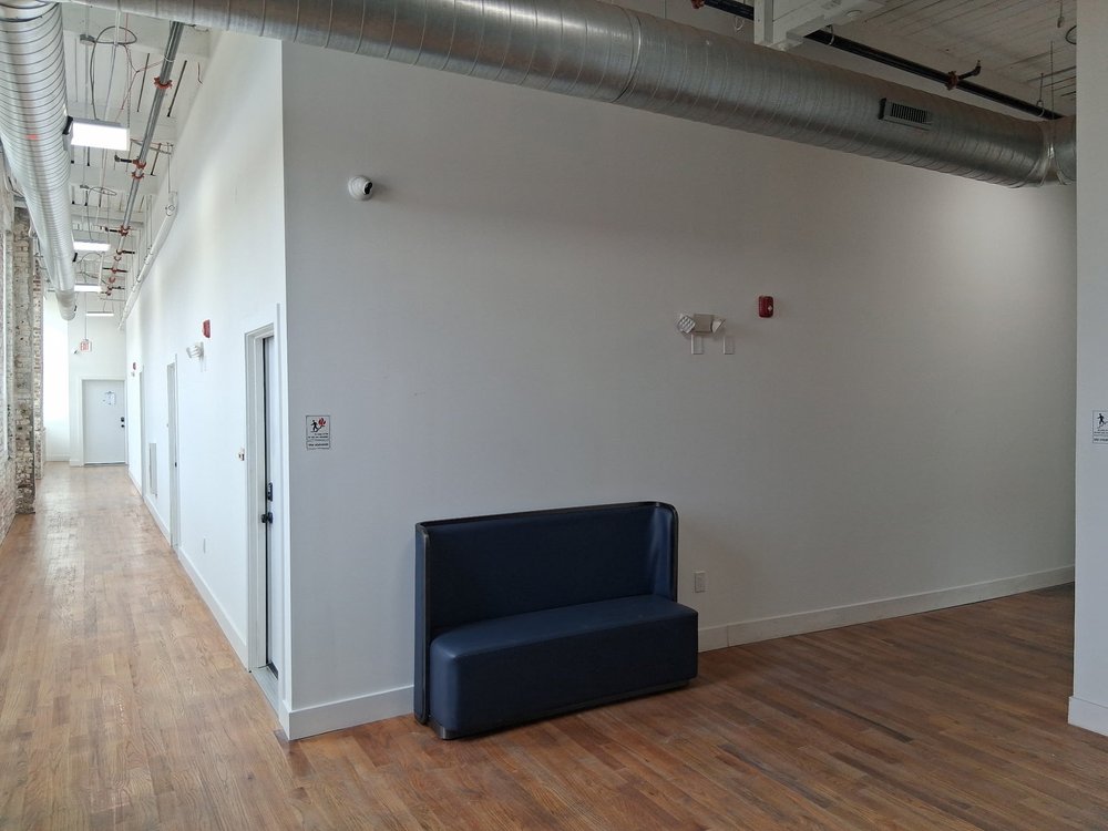 High-ceilinged common corridor with exposed conduit and seating at D Street Studios Philadelphia