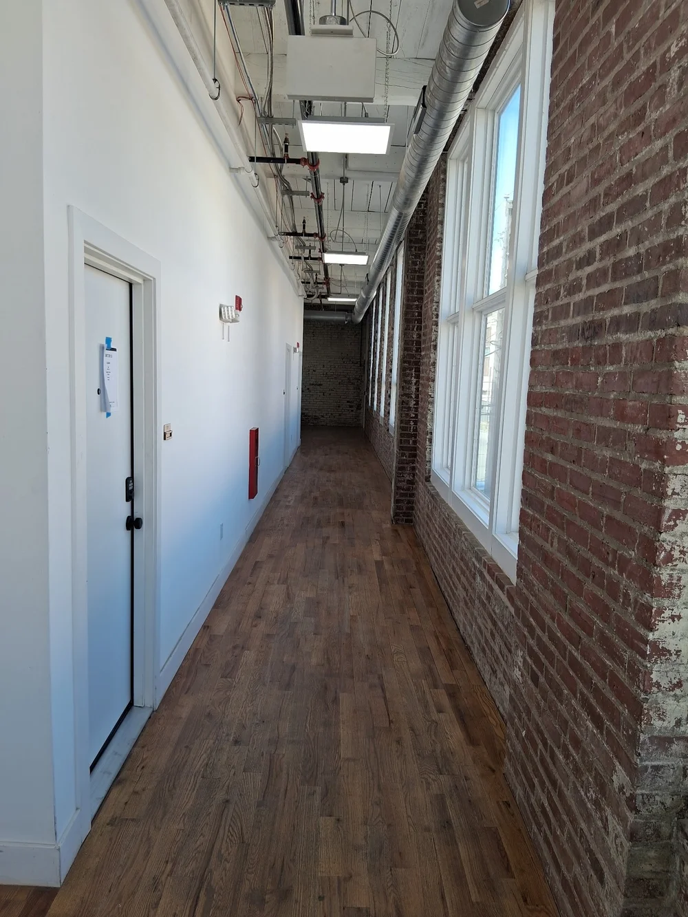 Studio corridor with tall factory windows, exposed brick and original wood plank floors at D Street Studios
