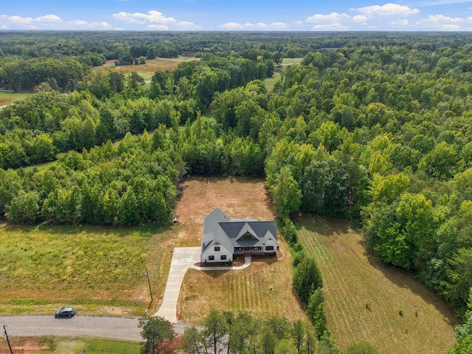 Aerial view of the white farmhouse-style home on its private wooded homesite in Summerfield
