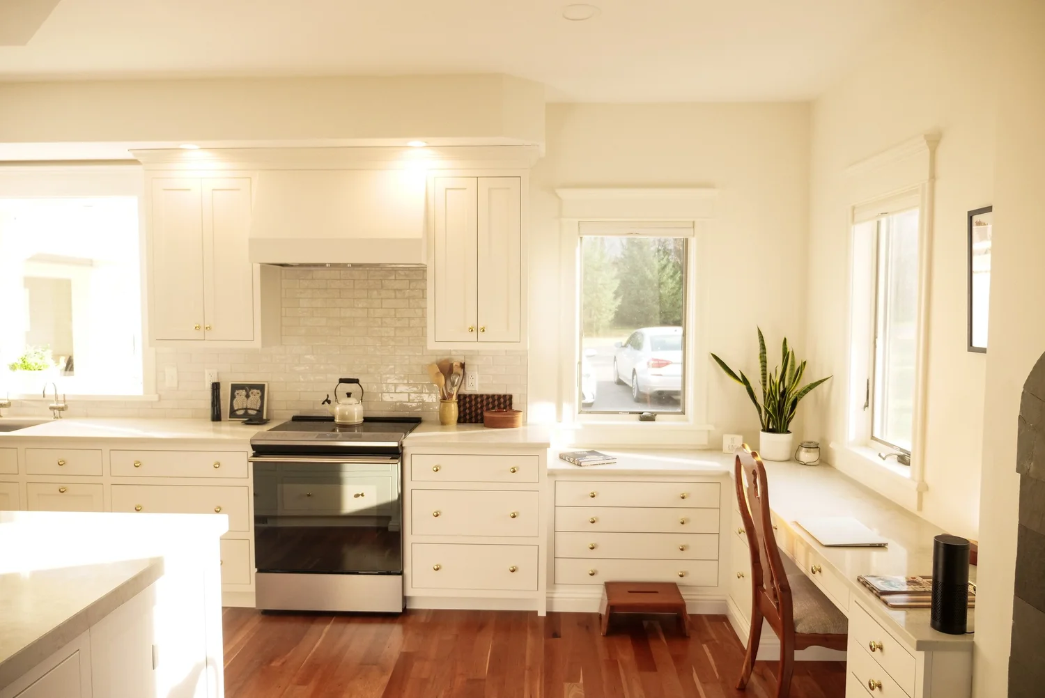 White kitchen cabinetry, range and built-in desk nook with hardwood floors