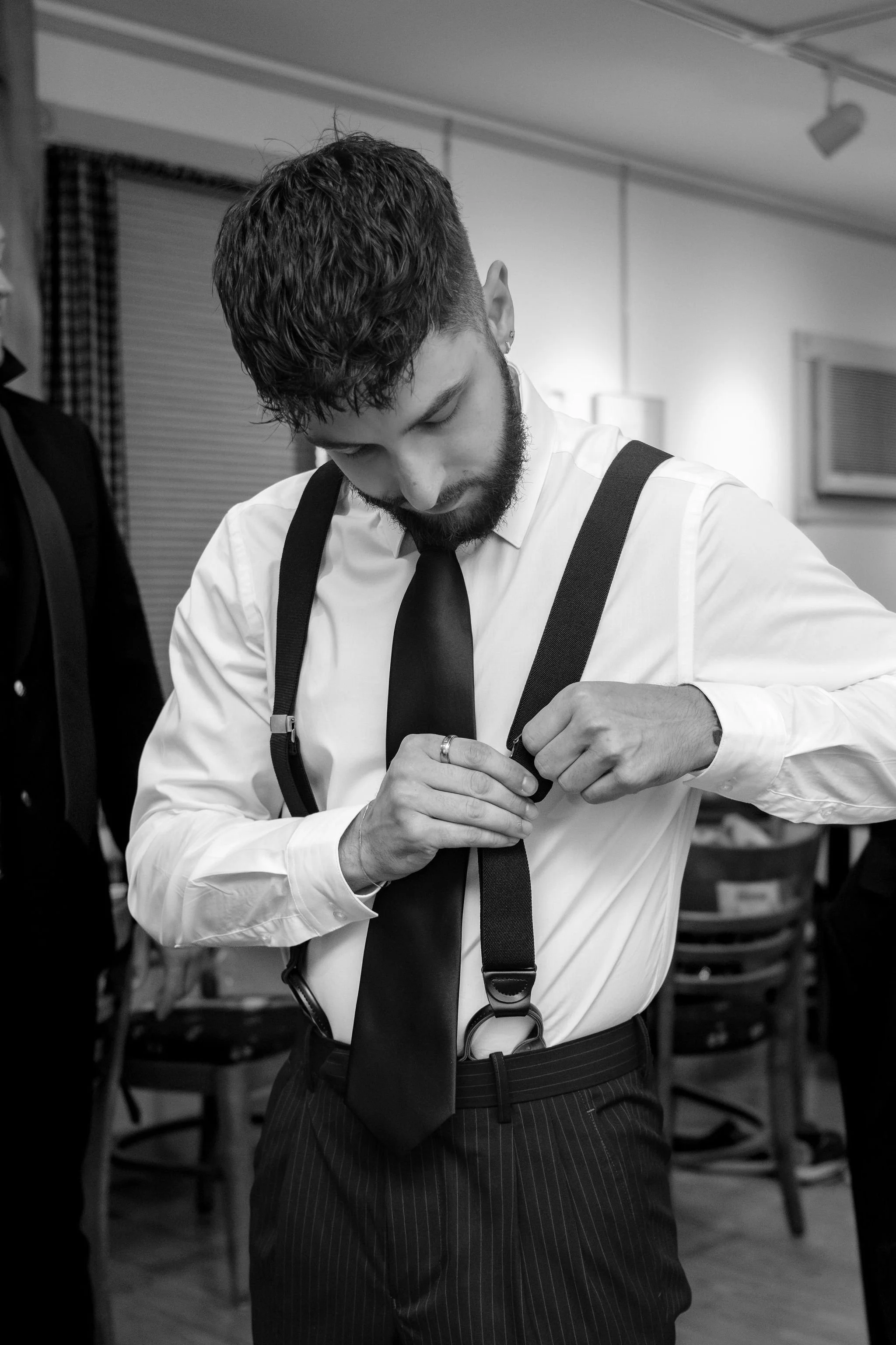Chase Begin fastening his suspenders while getting ready in black and white at Maple Hill Farm Inn and Conference Center in Hallowell Maine summer wedding photography VMG Productions