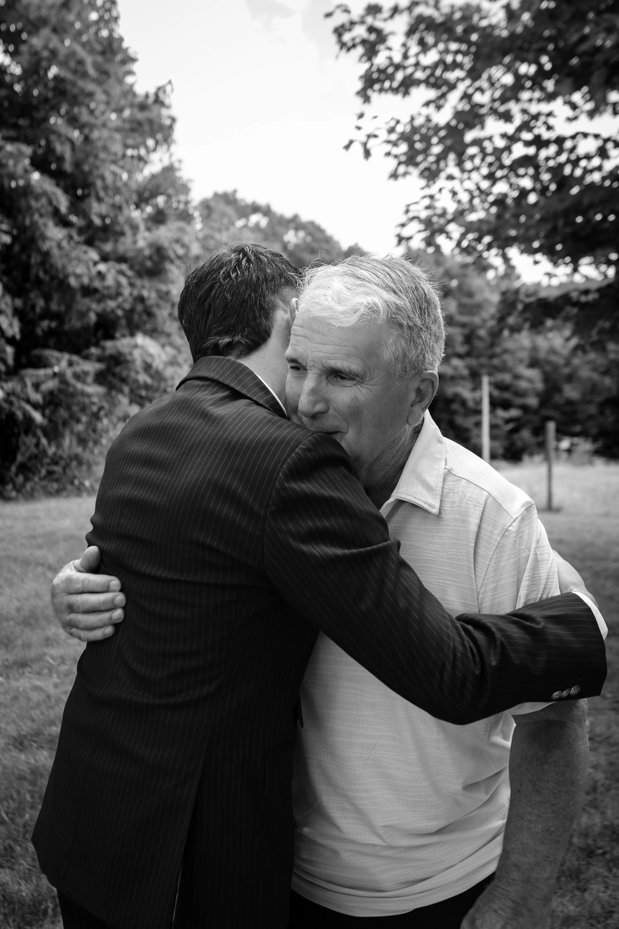 Chase Begin in a long hug with family after the ceremony in black and white at Maple Hill Farm Inn and Conference Center in Hallowell Maine summer wedding photography VMG Productions