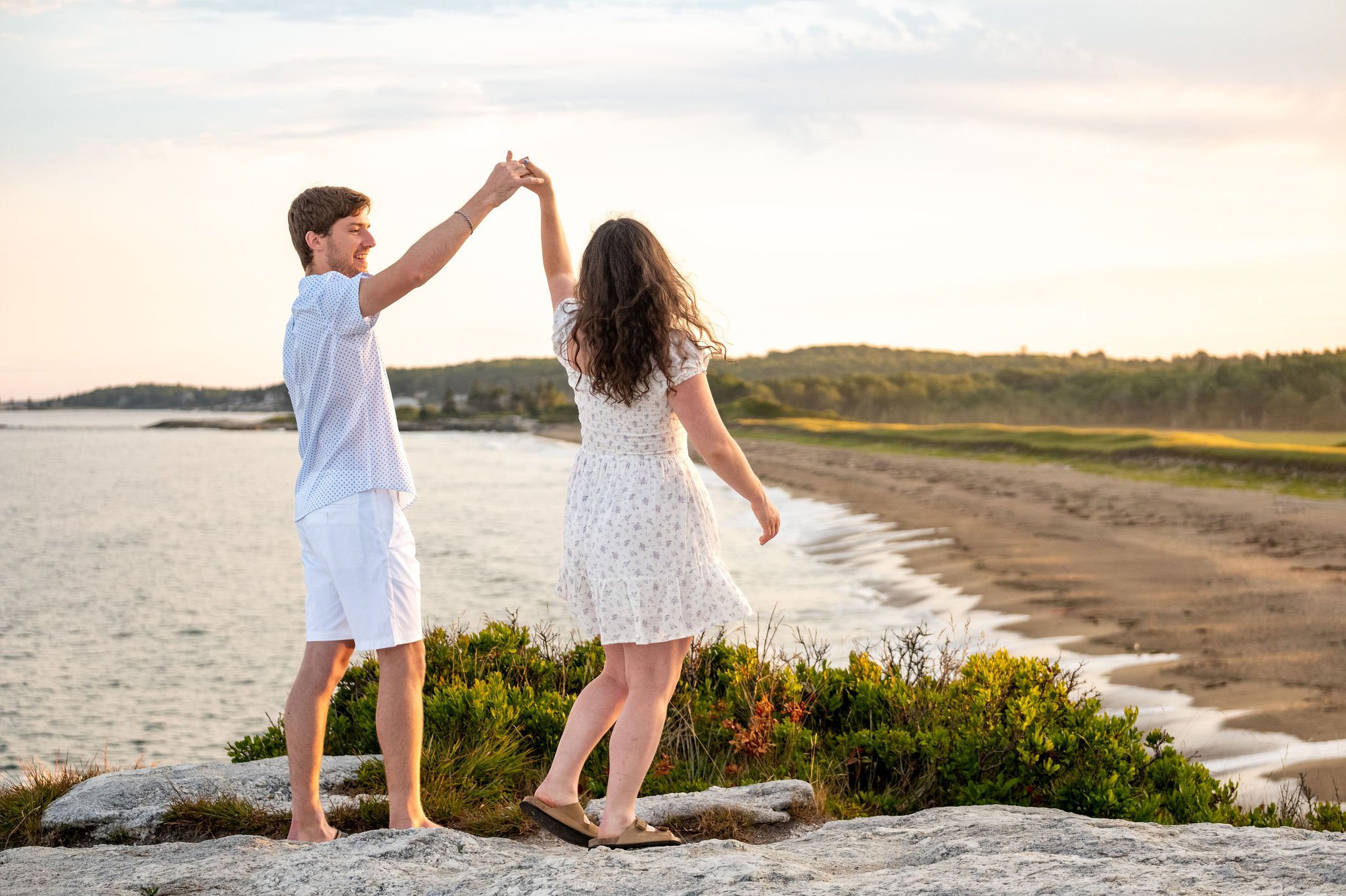 Lucas twirling Kirstie on the rocks above the beach at Reid State Park in Georgetown Maine engagement photography VMG Productions