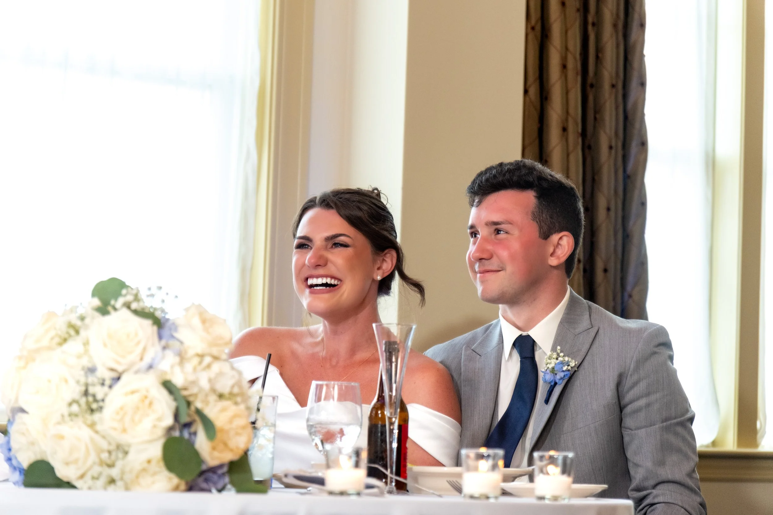 Caroline Pirolli laughing and Anthony holding back tears at the sweetheart table during a speech at Union Bluff Hotel in York Maine wedding photography VMG Productions