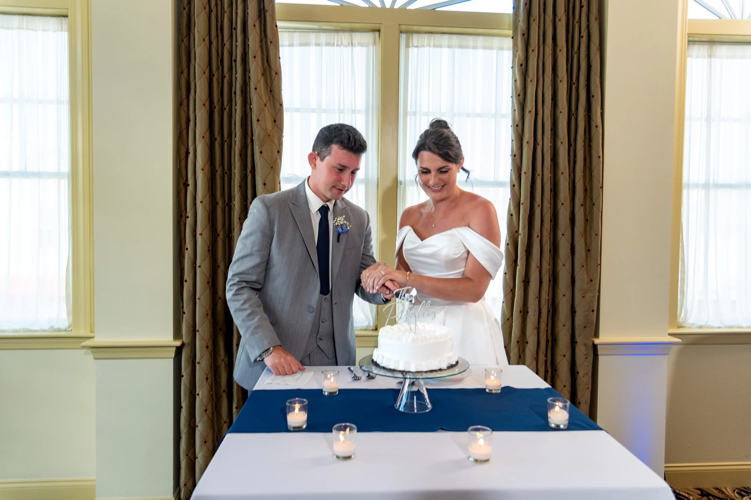 Caroline and Anthony Pirolli cutting their wedding cake together beside the tall windows at Union Bluff Hotel in York Maine wedding photography VMG Productions