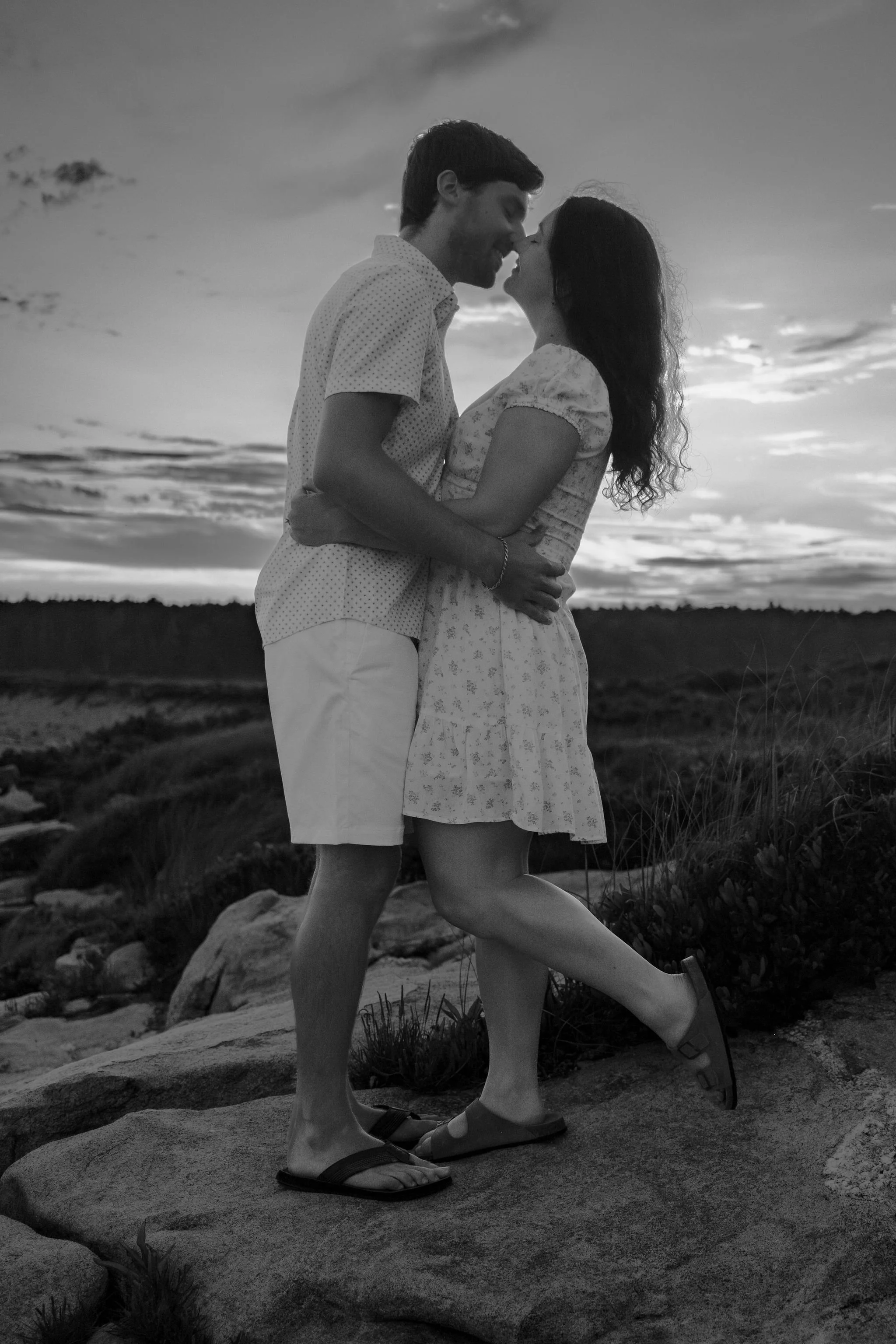 Kirstie and Lucas kissing at dusk on the rocks in black and white at Reid State Park in Georgetown Maine engagement photography VMG Productions