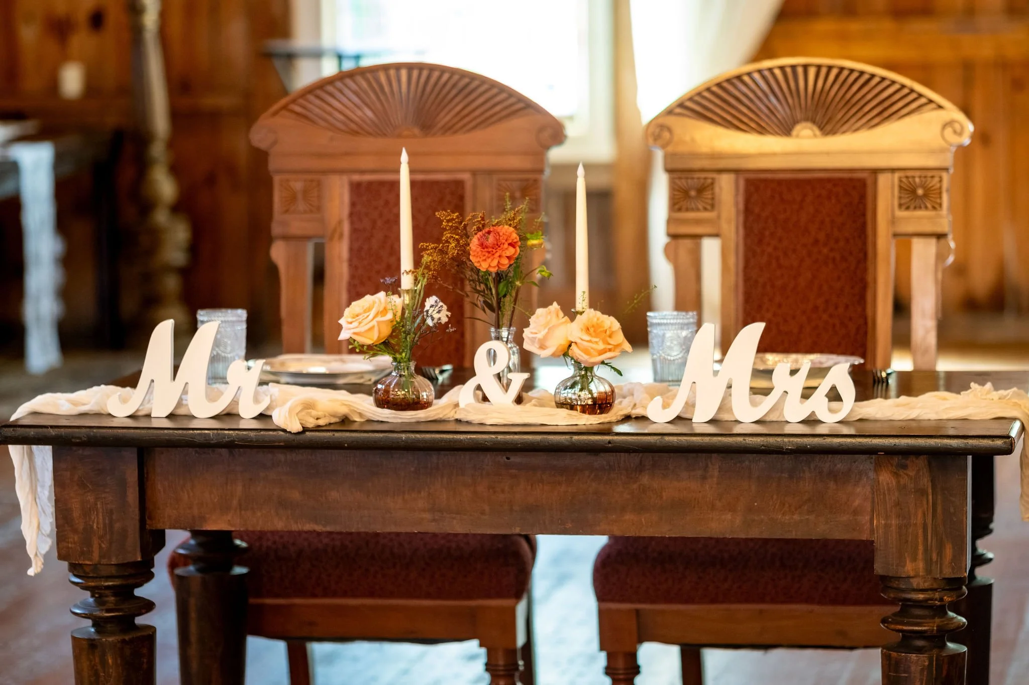 The sweetheart table with carved wooden chairs, candles, and a Mr and Mrs sign at Boothbay Playhouse in Boothbay Maine fall wedding photography VMG Productions