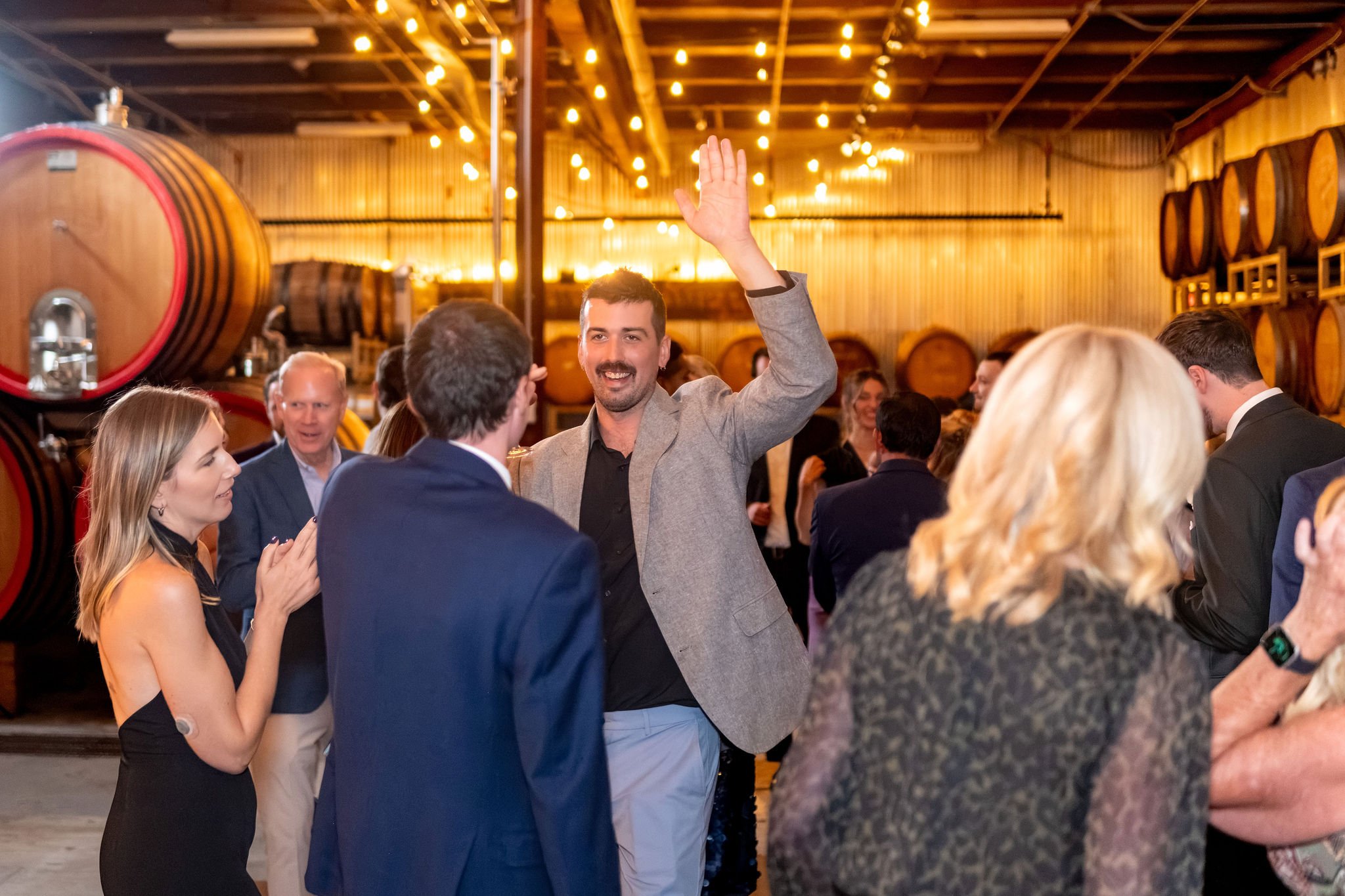 Guests dancing under the string lights of the barrel room with one guest throwing a hand in the air at The Cellars at Allagash Brewing Company in Portland Maine fall wedding photography VMG Productions