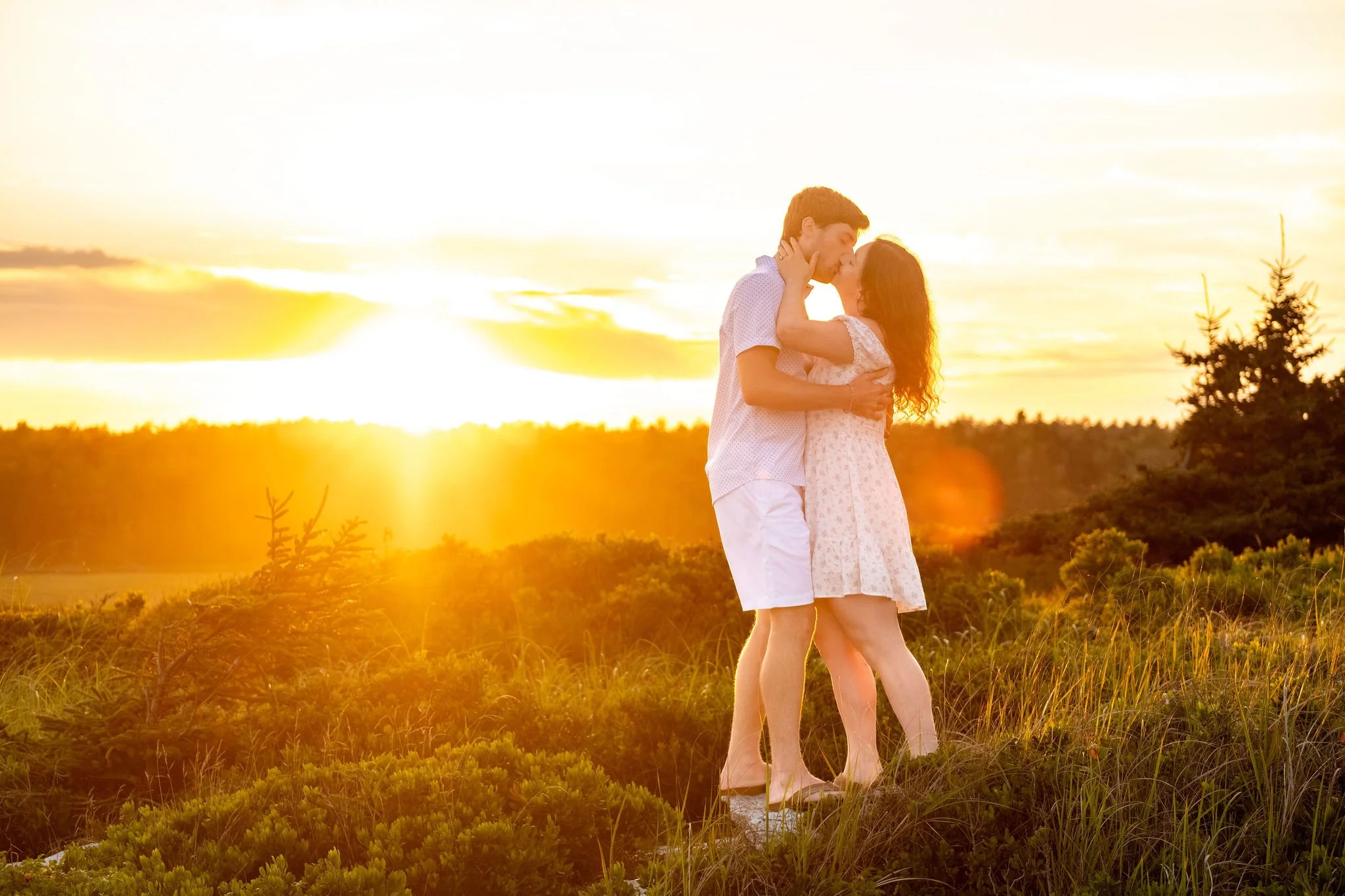 Kirstie and Lucas embracing with the setting sun bursting through the spruce behind them at Reid State Park in Georgetown Maine engagement photography VMG Productions