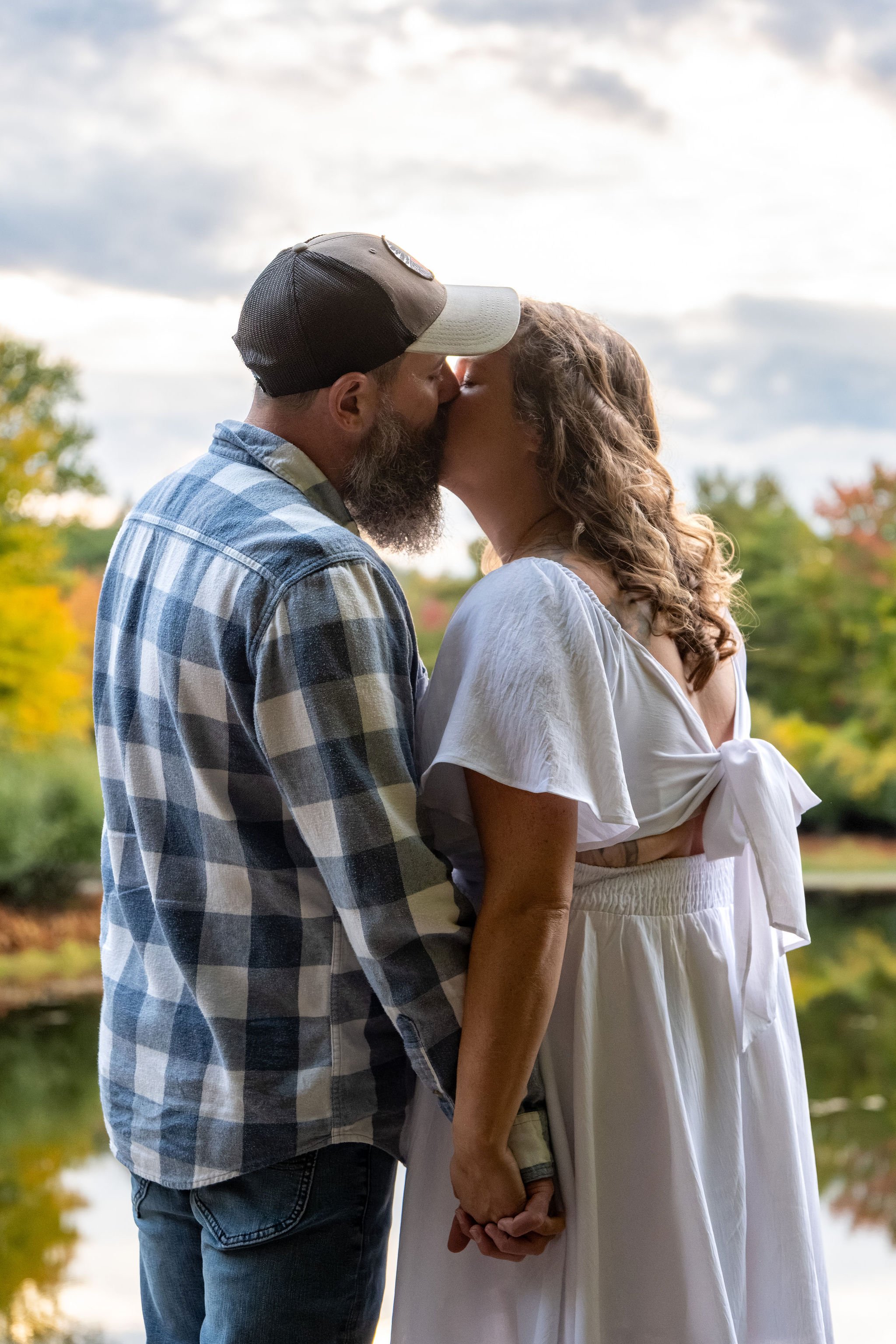Alison and Dave kissing at the pond's edge with the sky opening up behind them at Vaughan Woods in Hallowell Maine fall engagement photography VMG Productions