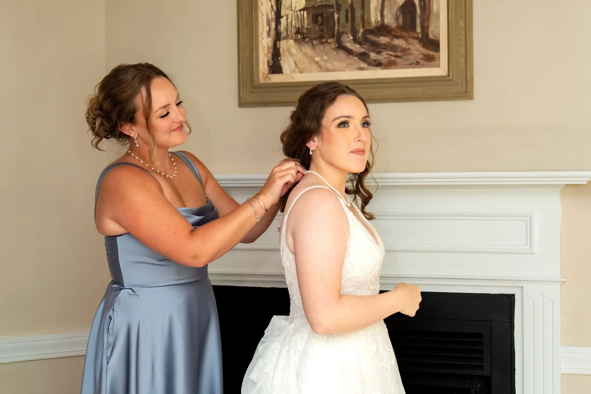 A bridesmaid in dusty blue fastening Hollie's pearl necklace before the ceremony at The Lucerne Inn in Dedham Maine summer wedding photography VMG Productions