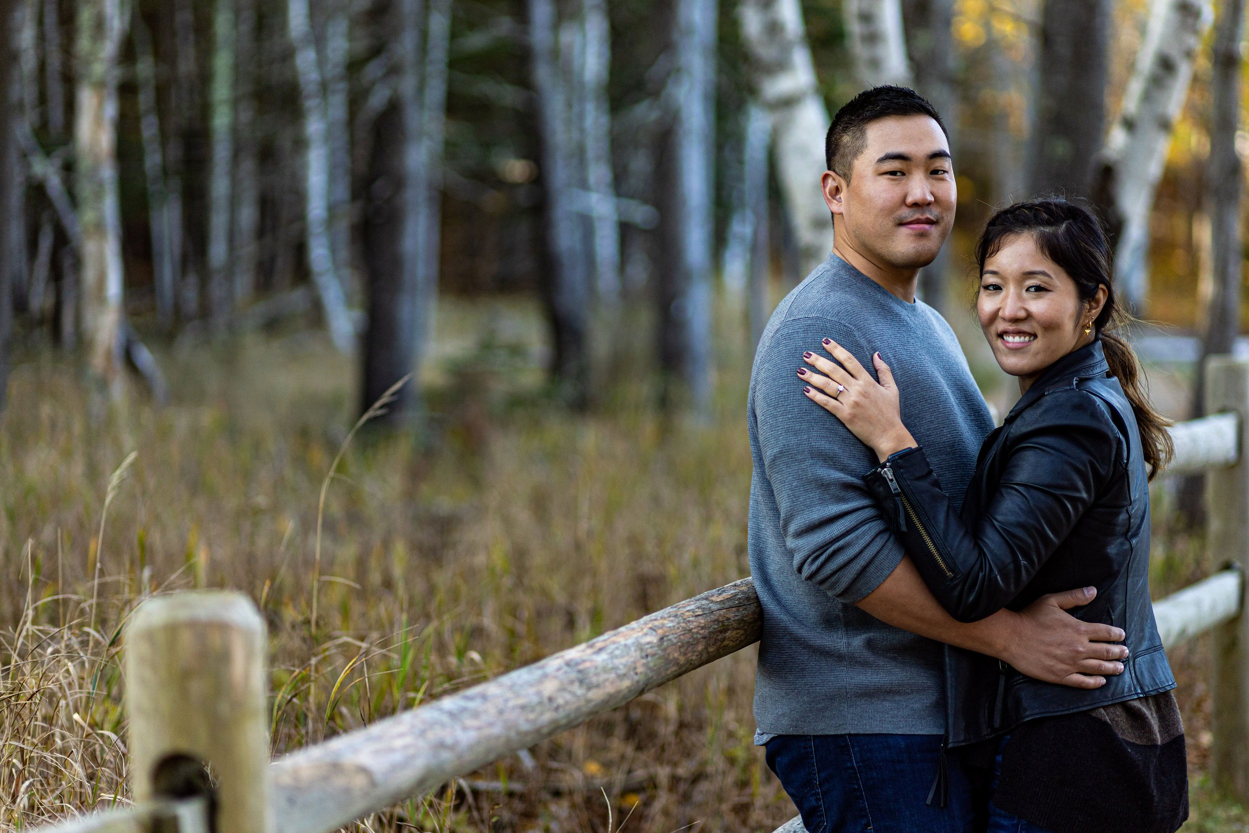Agnes and Peter standing embrace by split-rail fence birch forest Acadia National Park engagement photography VMG Productions