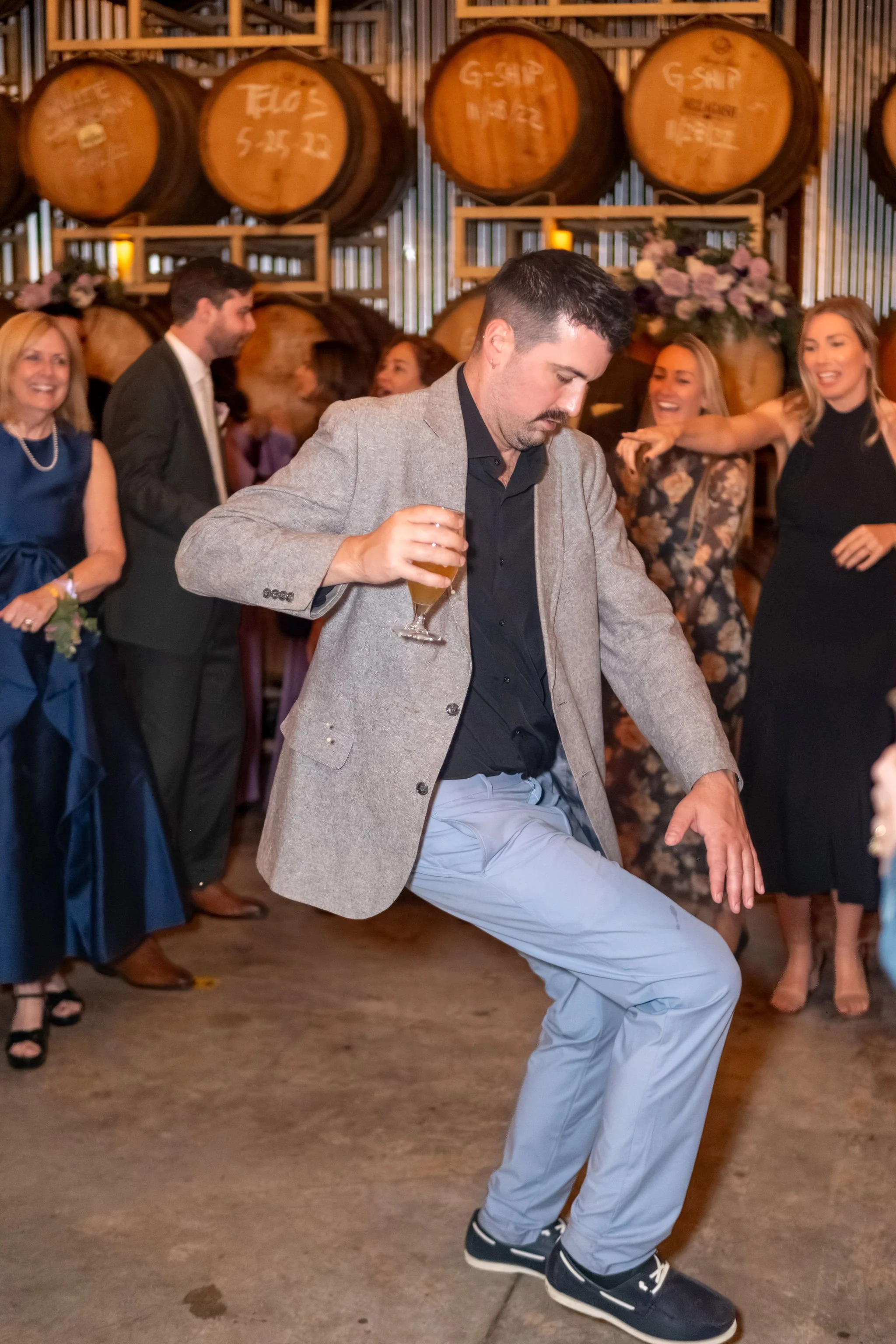 A guest in a gray blazer showing off his dance moves with a beer in hand at The Cellars at Allagash Brewing Company in Portland Maine fall wedding photography VMG Productions