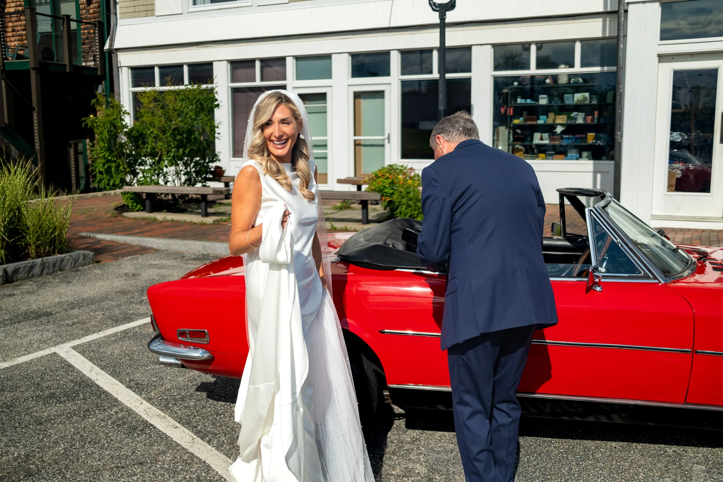 Ashley Draper laughing beside the vintage red Fiat convertible as her father Ernie readies it for the ride to the ceremony at The Breakwater Inn in Kennebunkport Maine summer wedding photography VMG Productions