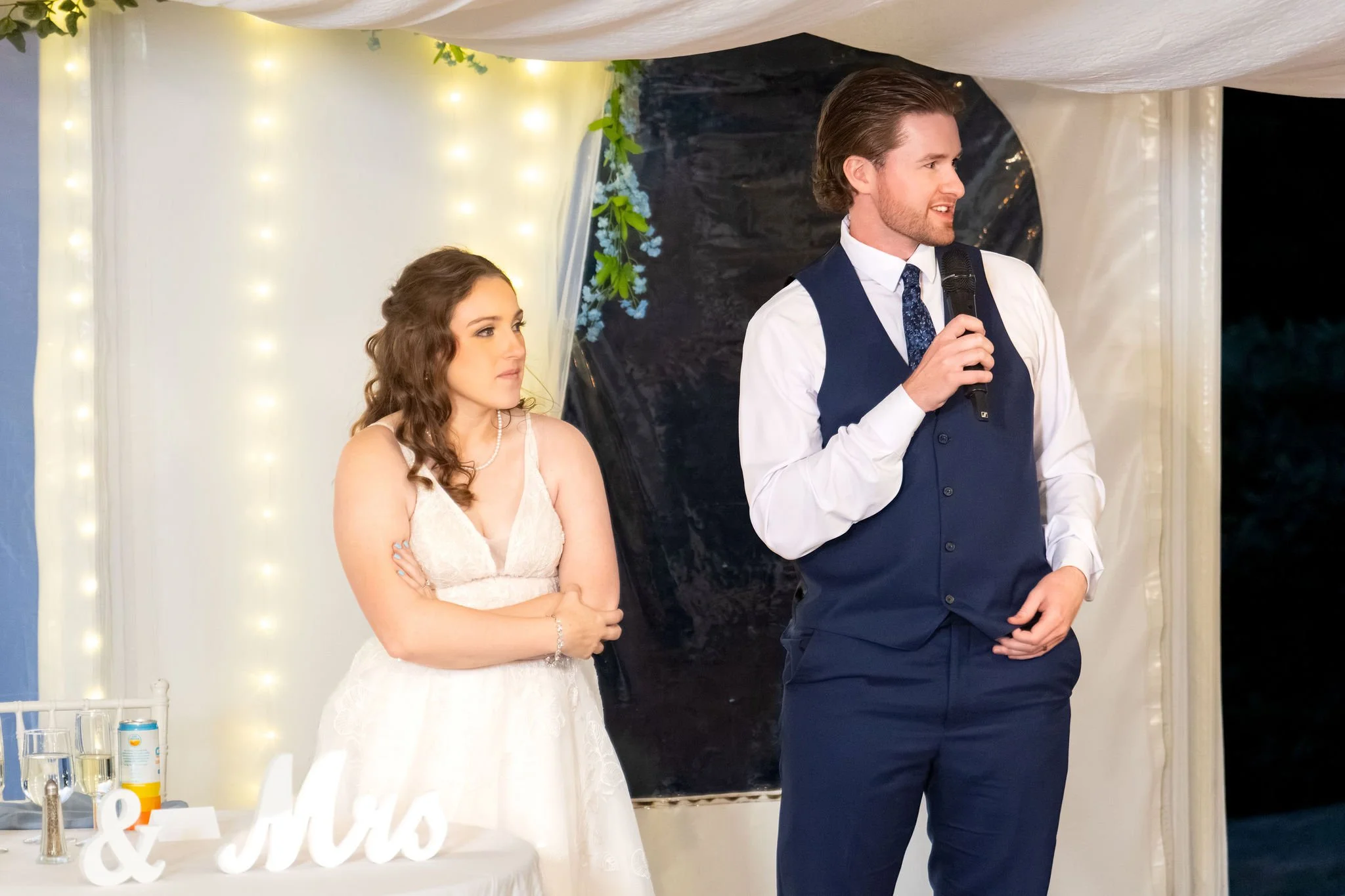 Zachary speaking into a microphone with Hollie beside him as they thank their guests from the head table at The Lucerne Inn in Dedham Maine summer wedding photography VMG Productions