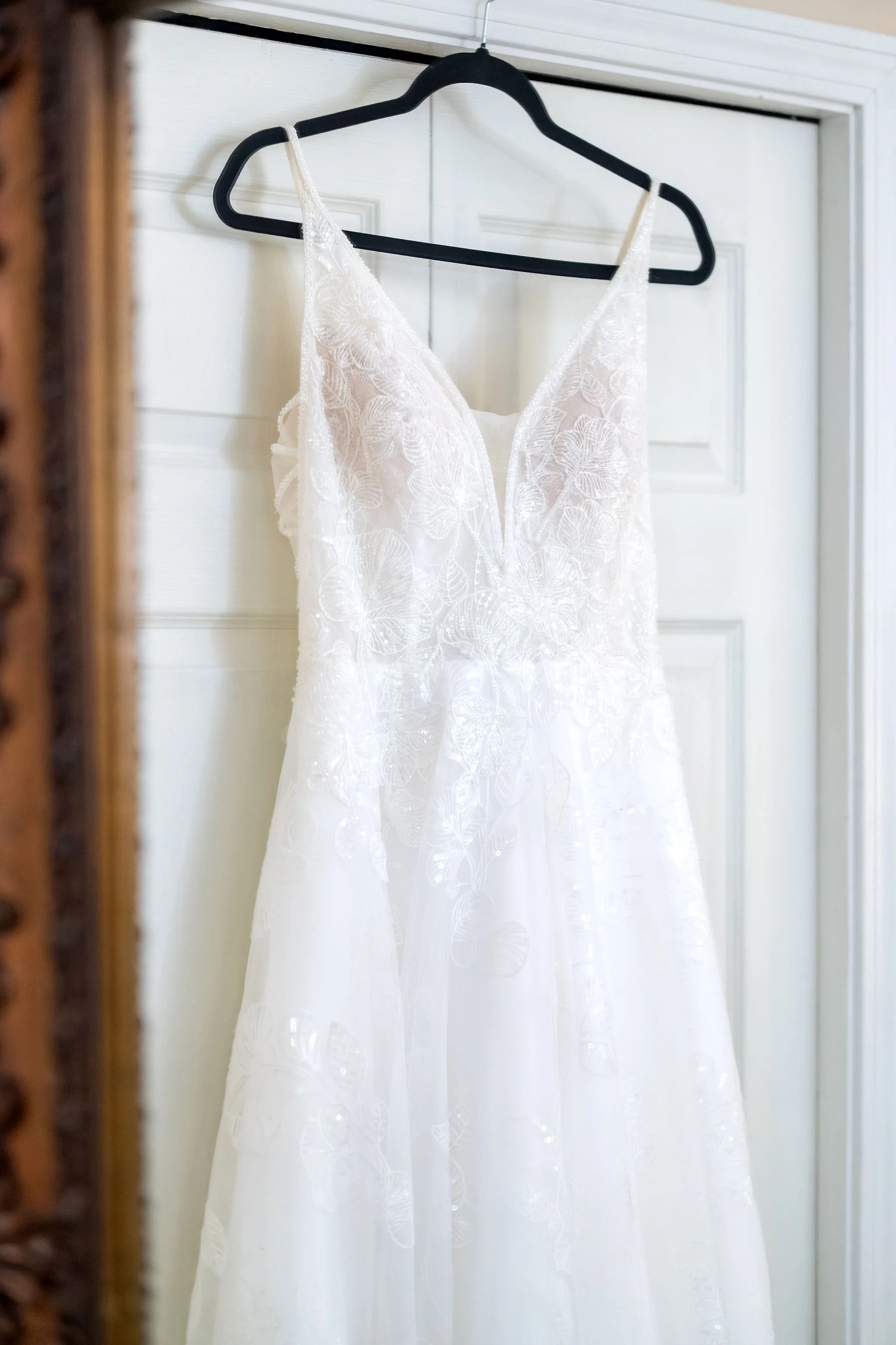 Close view of the beaded bodice of Hollie's wedding gown hanging on a white door at The Lucerne Inn in Dedham Maine summer wedding photography VMG Productions