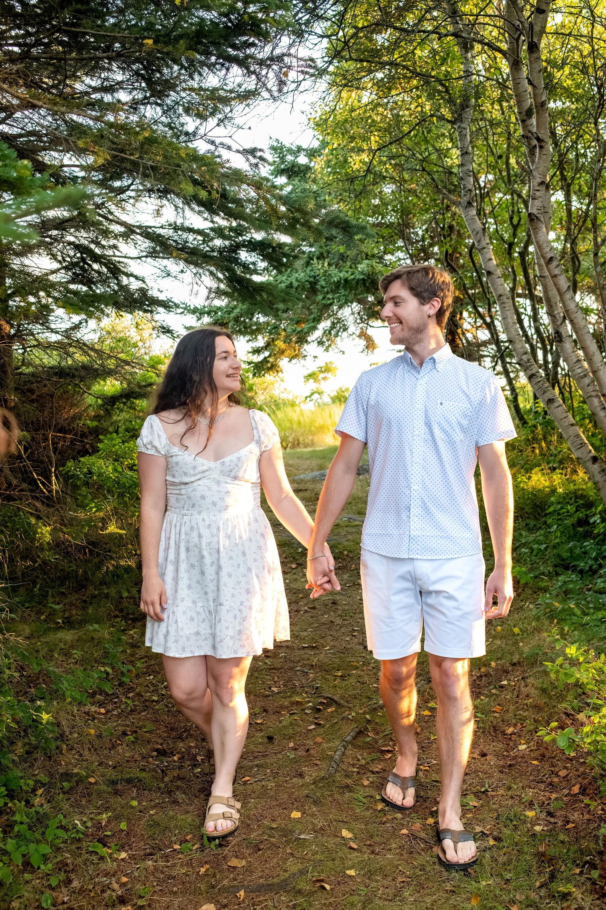 Kirstie and Lucas walking toward the camera hand in hand on the path through the trees at Reid State Park in Georgetown Maine engagement photography VMG Productions