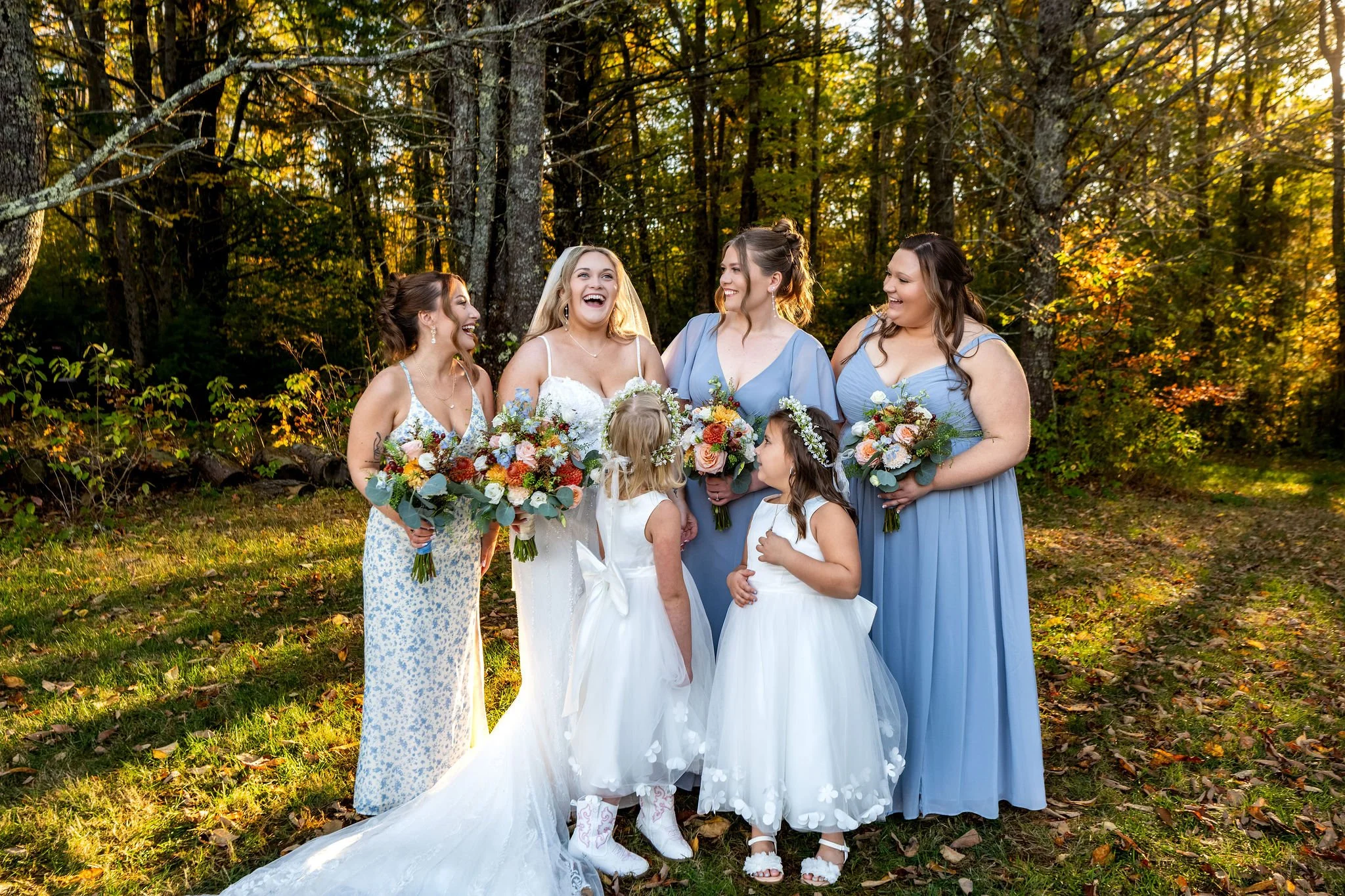 Ellie laughing with her bridesmaids and flower girls in the fall woods at Boothbay Playhouse in Boothbay Maine fall wedding photography VMG Productions