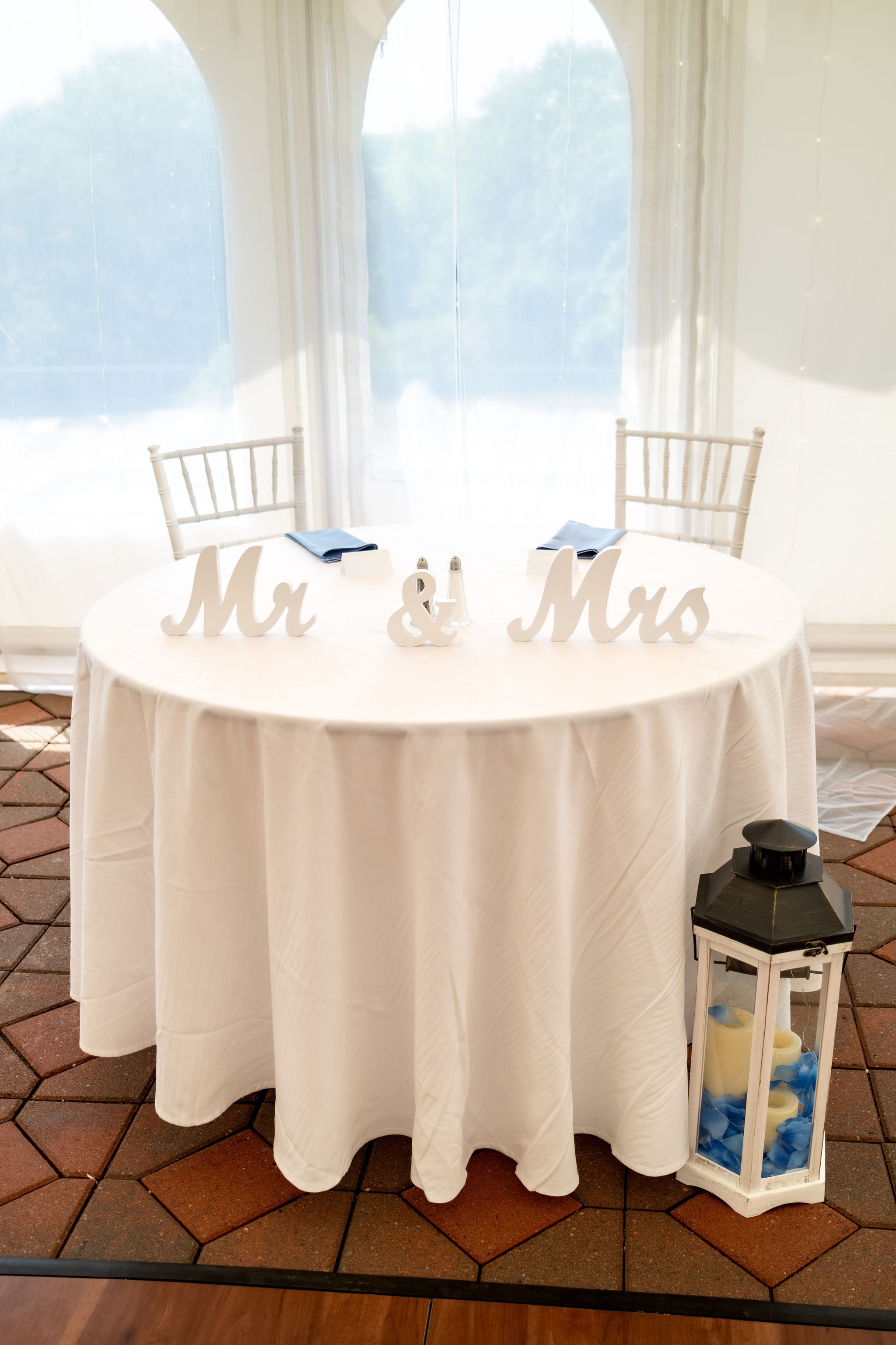 Mr and Mrs sweetheart table with a white lantern and blue hydrangeas under the reception tent at The Lucerne Inn in Dedham Maine summer wedding photography VMG Productions