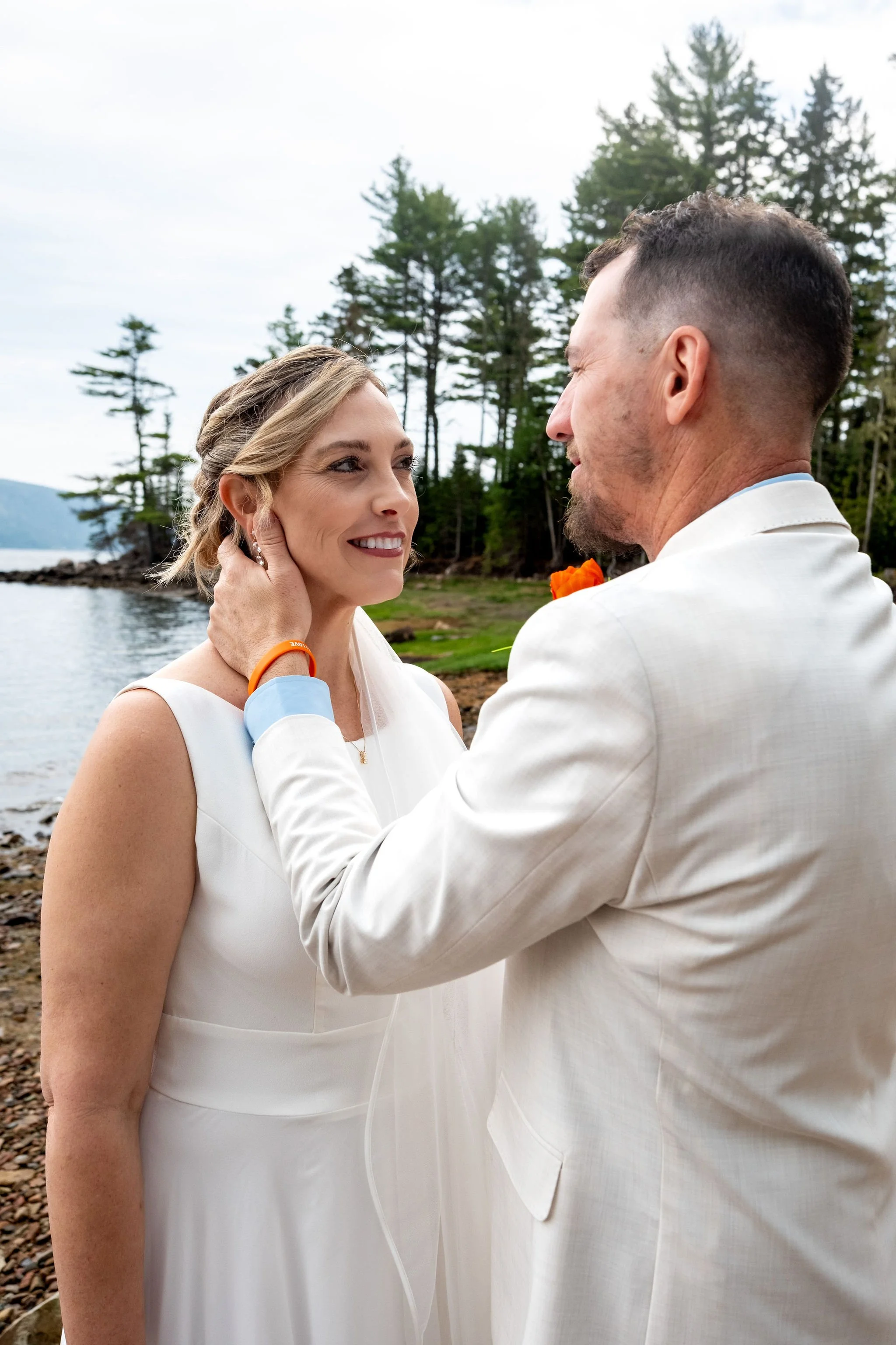Alli and Adam Baudoin smiling at each other at the water's edge during their first look in Mount Desert Maine spring wedding photography VMG Productions