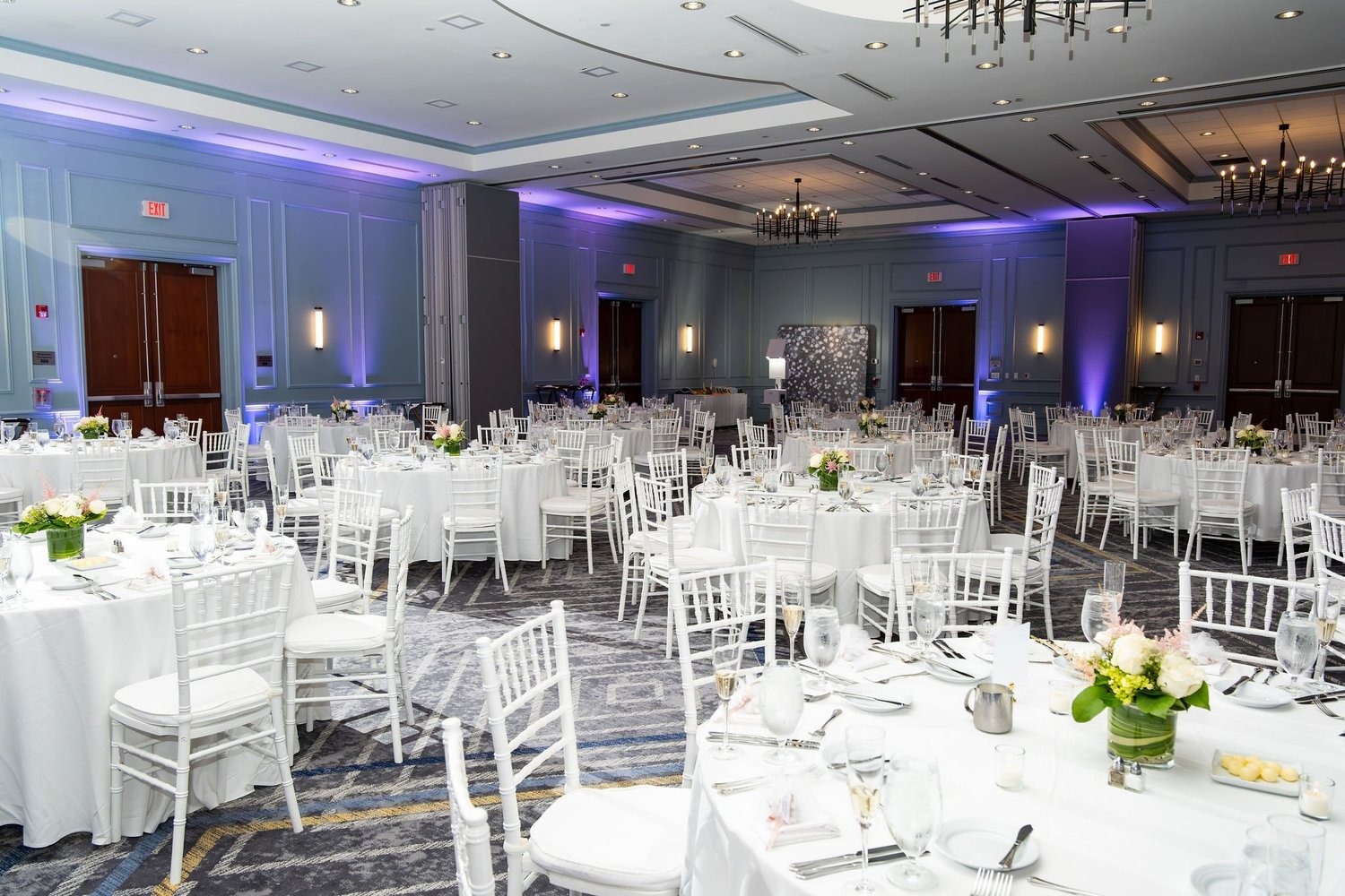 The ballroom set in white with purple uplighting for the reception at Portland Sheraton at Sable Oaks South Portland Maine summer wedding photography VMG Productions
