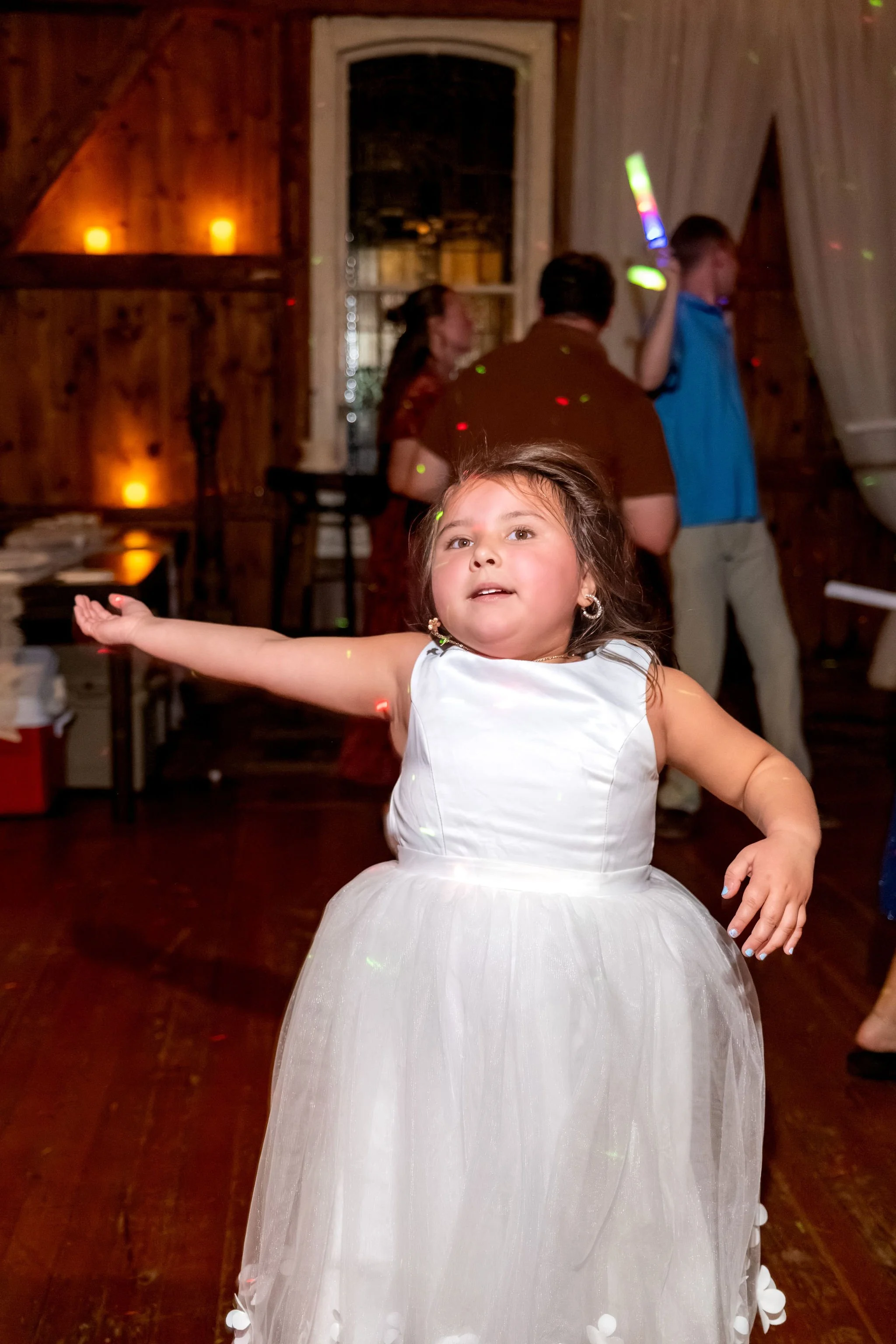A flower girl in a white dress dancing with her arms out on the barn floor at Boothbay Playhouse in Boothbay Maine fall wedding photography VMG Productions