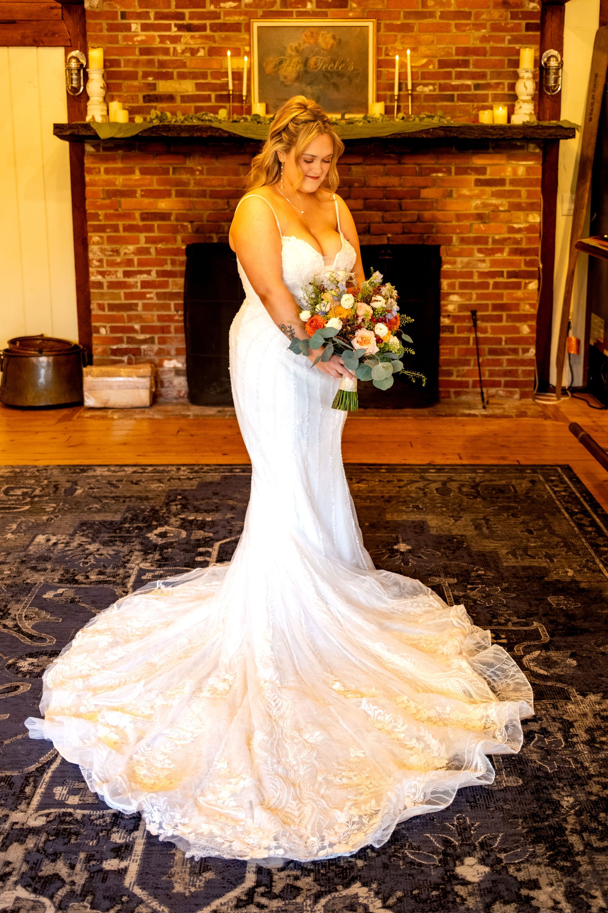 Ellie standing in front of the brick fireplace holding her bouquet with her gown flowing across the rug at Boothbay Playhouse in Boothbay Maine fall wedding photography VMG Productions